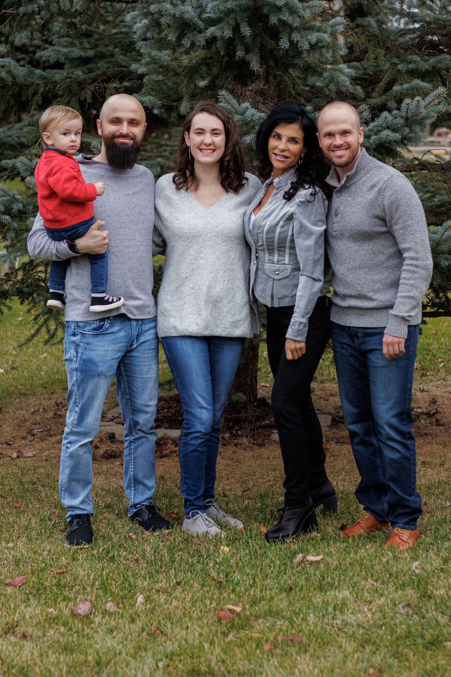 Casual family portrait outdoors with everyone wearing coordinating gray sweaters and jeans.