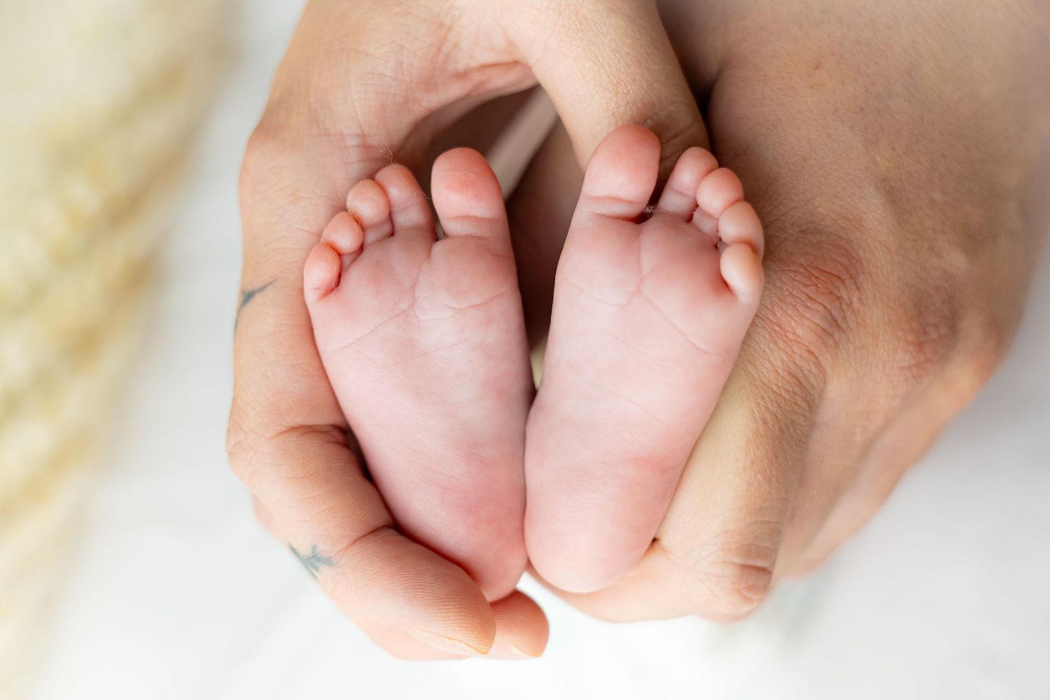 Newborn baby feet cradled in caring hands against white background.
