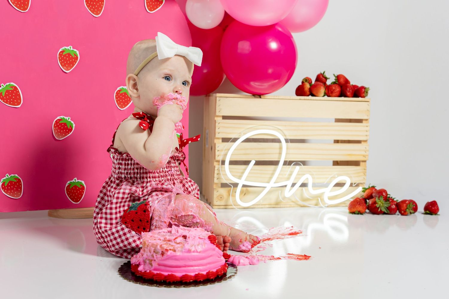 Strawberry themed party setup with pink balloons and wooden crate against white backdrop.