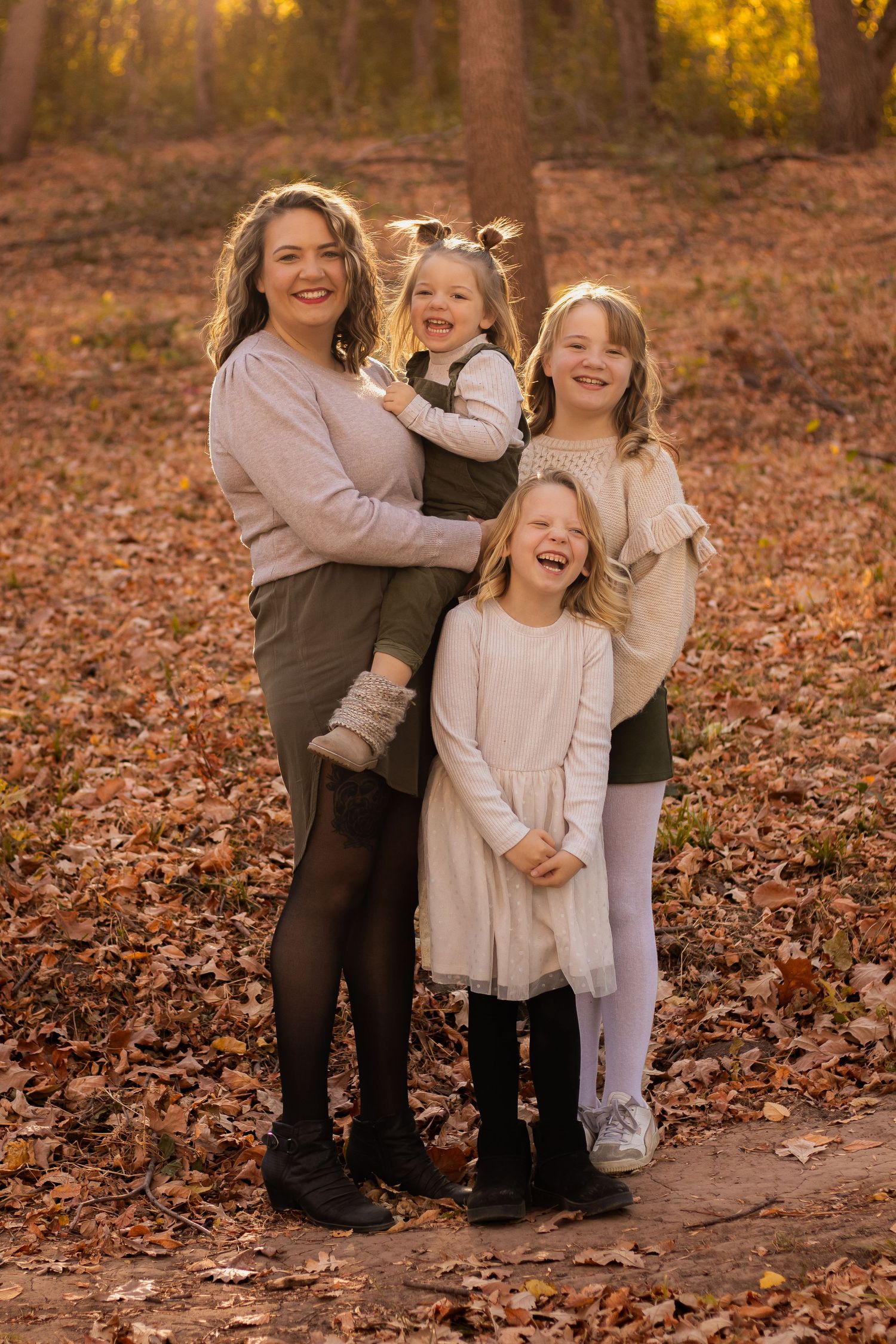 Fall family portrait with group embracing on leaf-covered ground in golden sunlight.