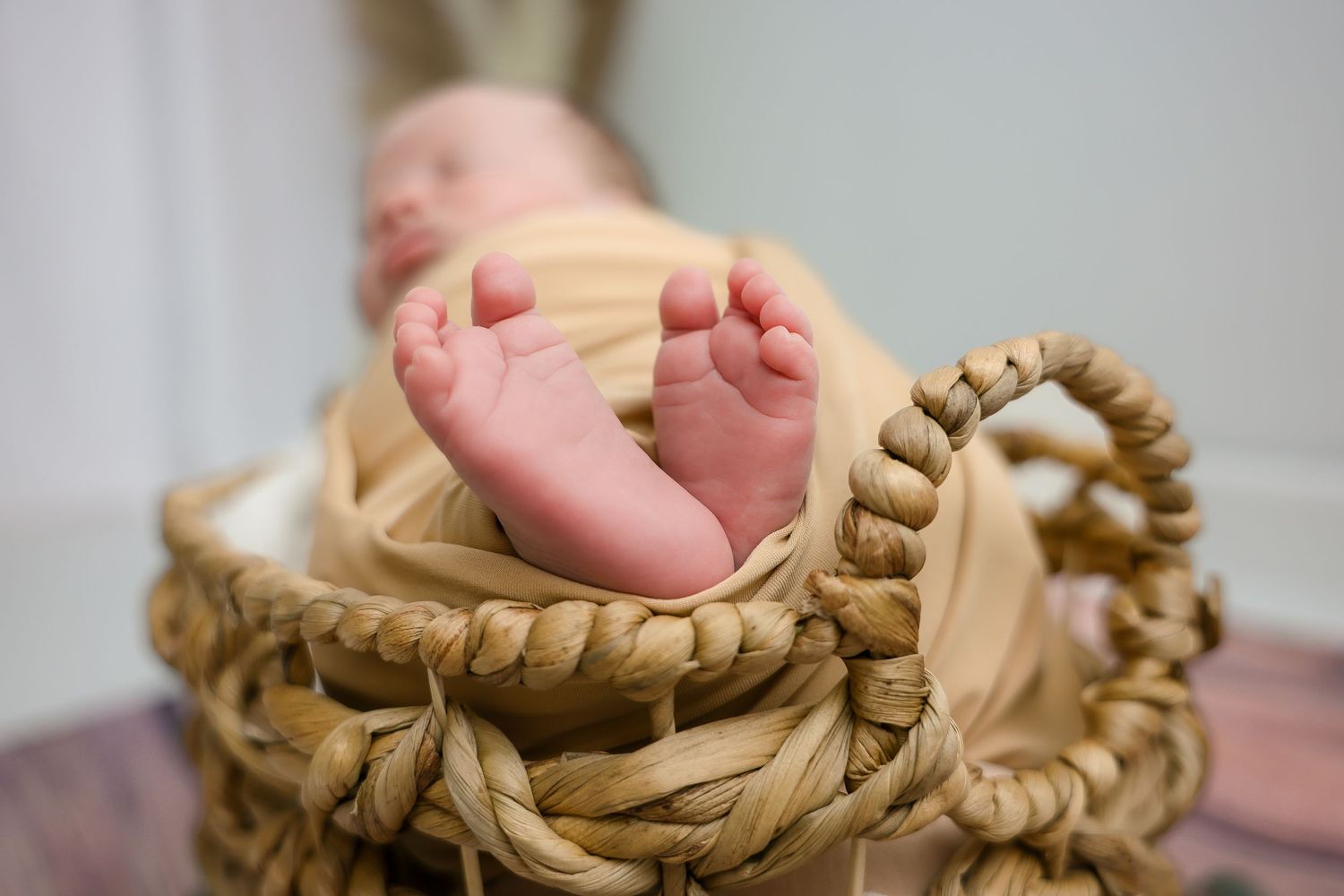 Tiny baby feet peek out from a woven basket with soft cream-colored fabric.