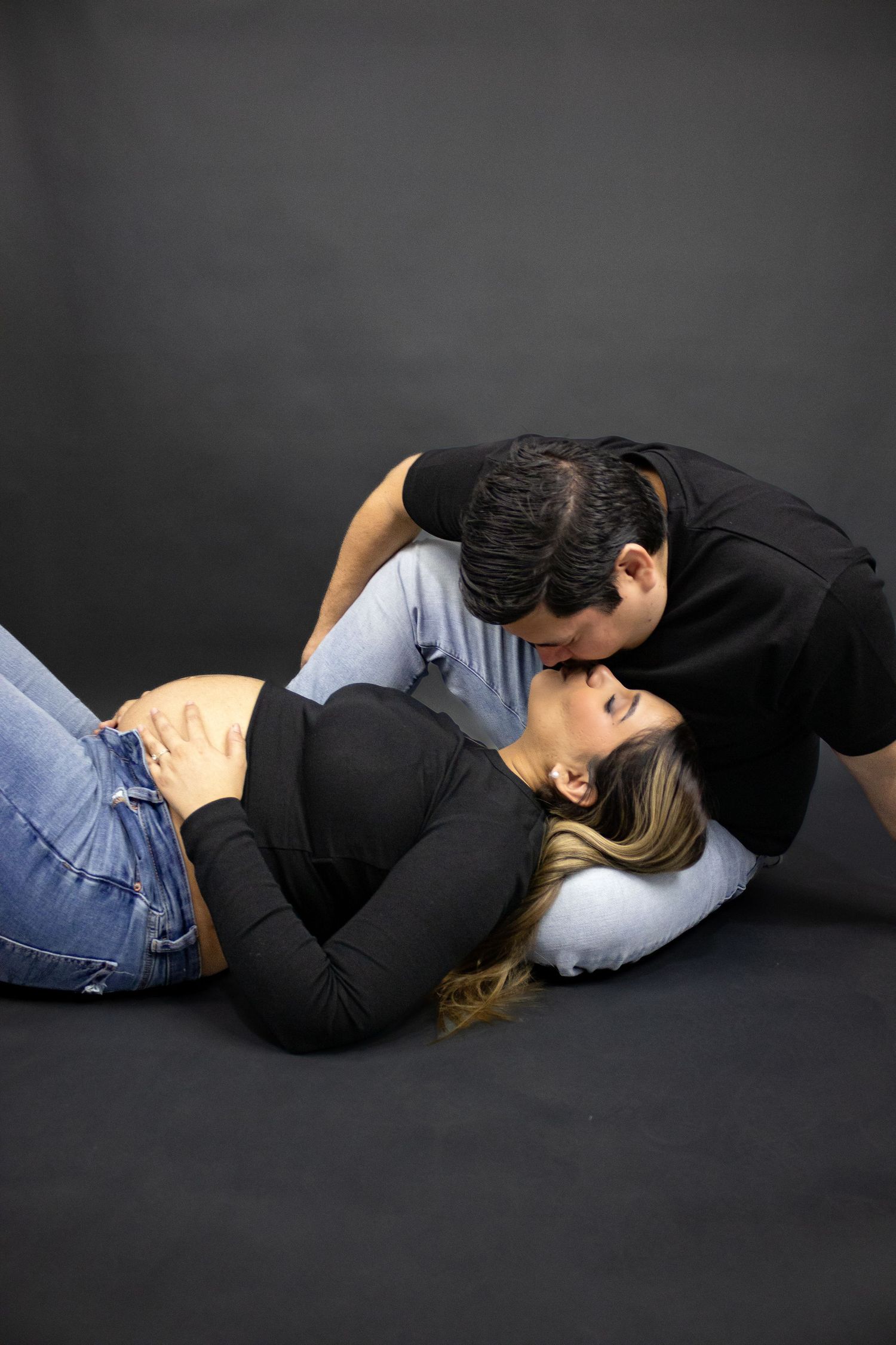 Couple in black and blue clothing embracing while lying on dark background in artistic portrait series.