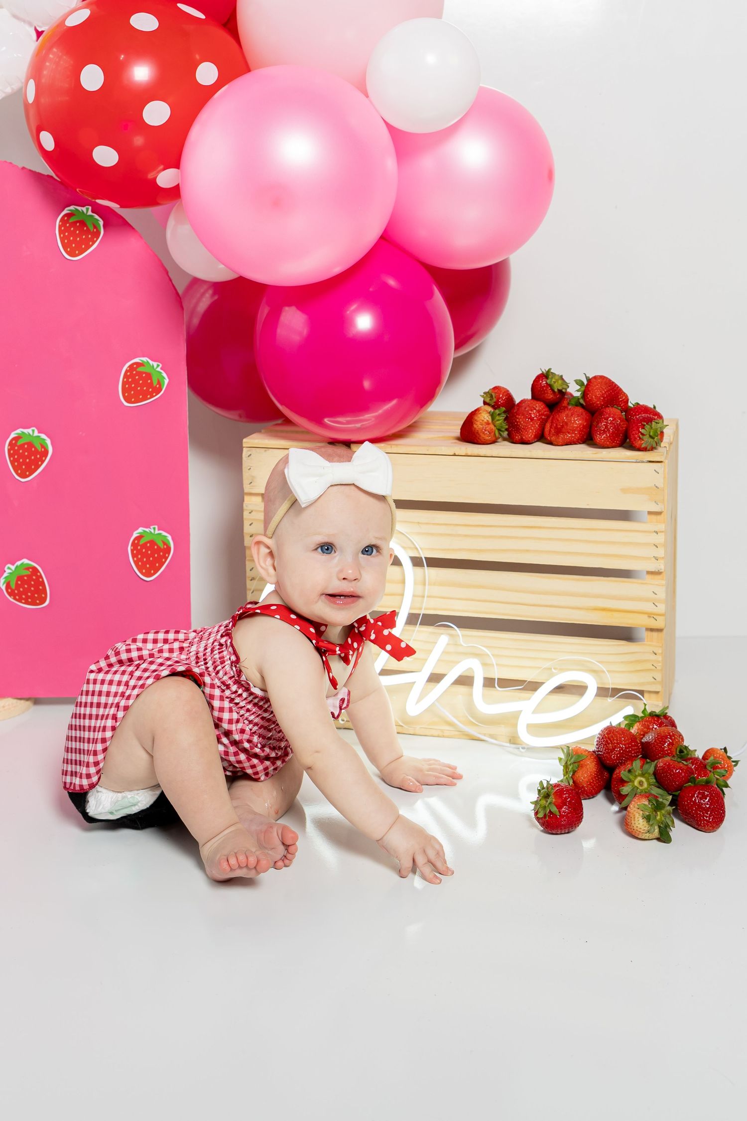 Strawberry themed photo setup with wooden crate, pink balloons, and polka dot decorations.