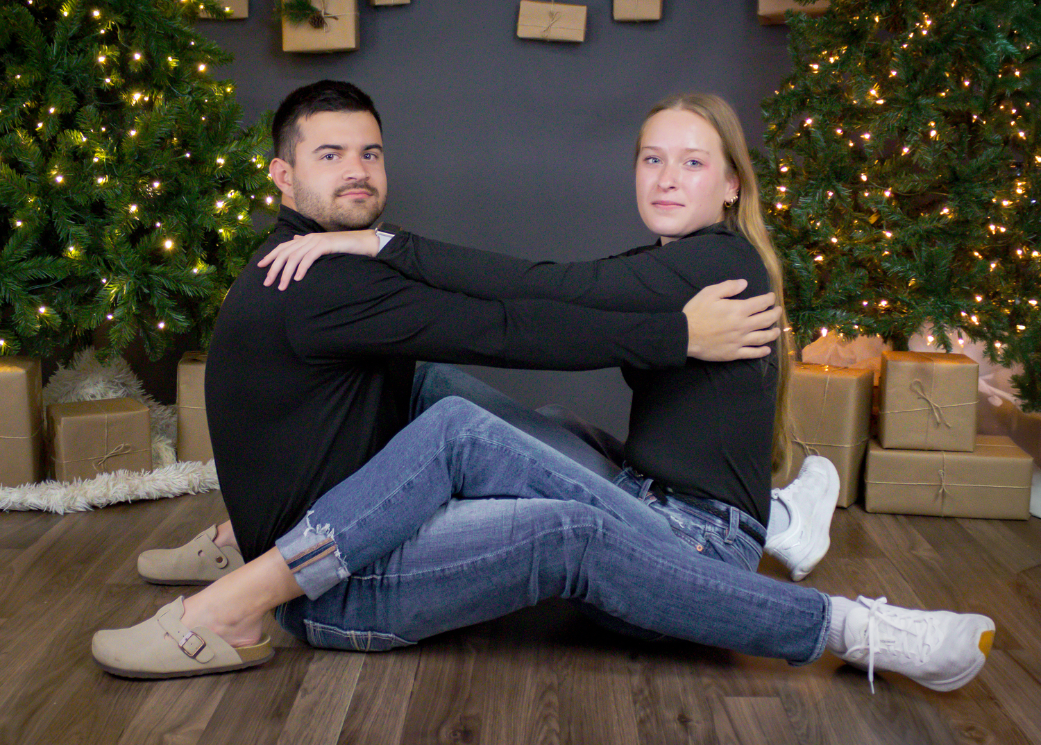 Couple lounging on hardwood floor with decorated Christmas tree and presents behind them.