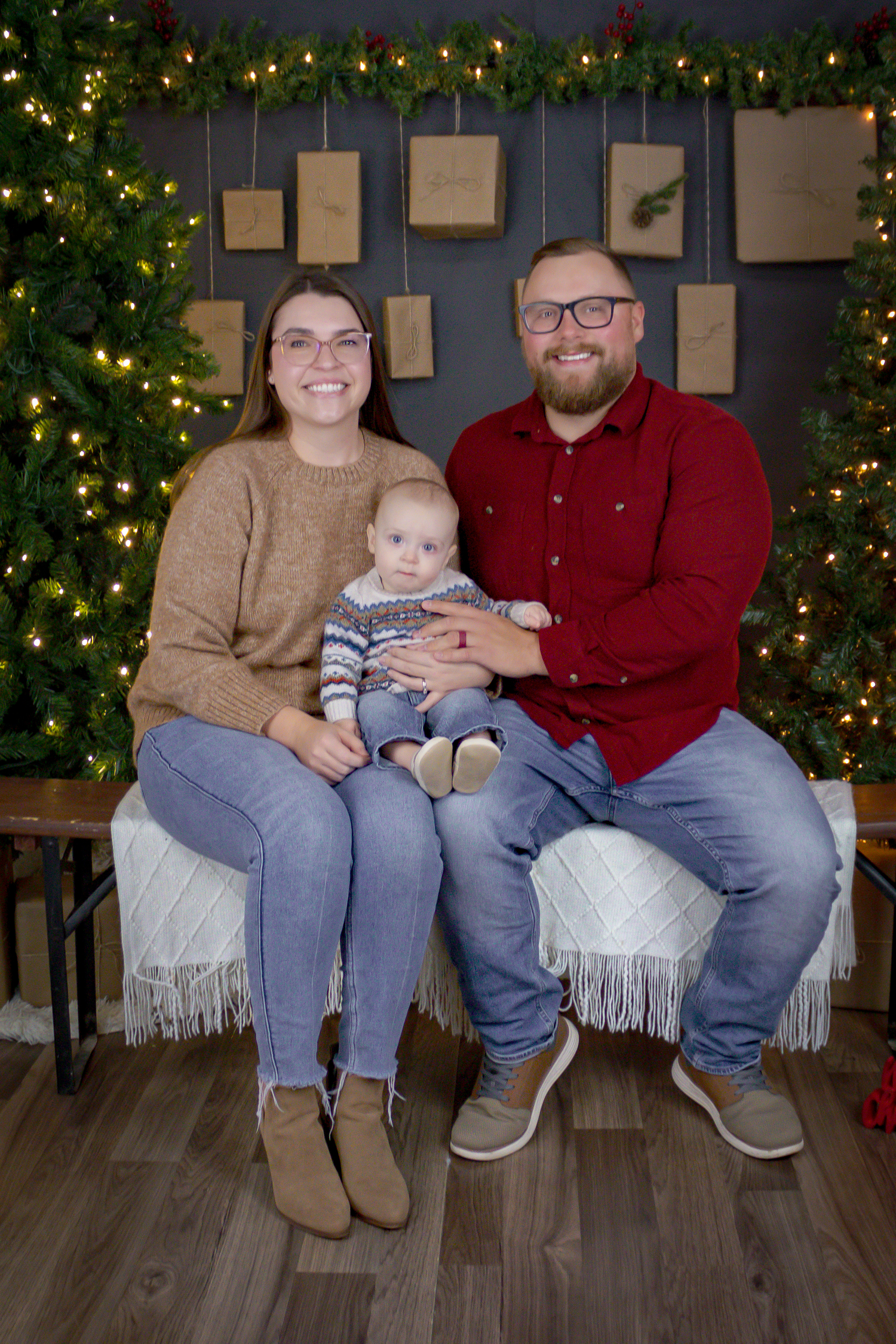 Family in cozy winter outfits poses on white bench for Christmas photos.