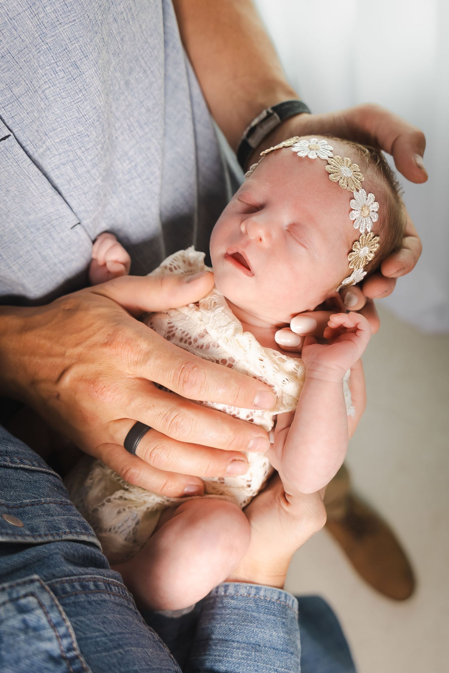 Gentle hands cradle a sleeping newborn wearing delicate lace accessories.