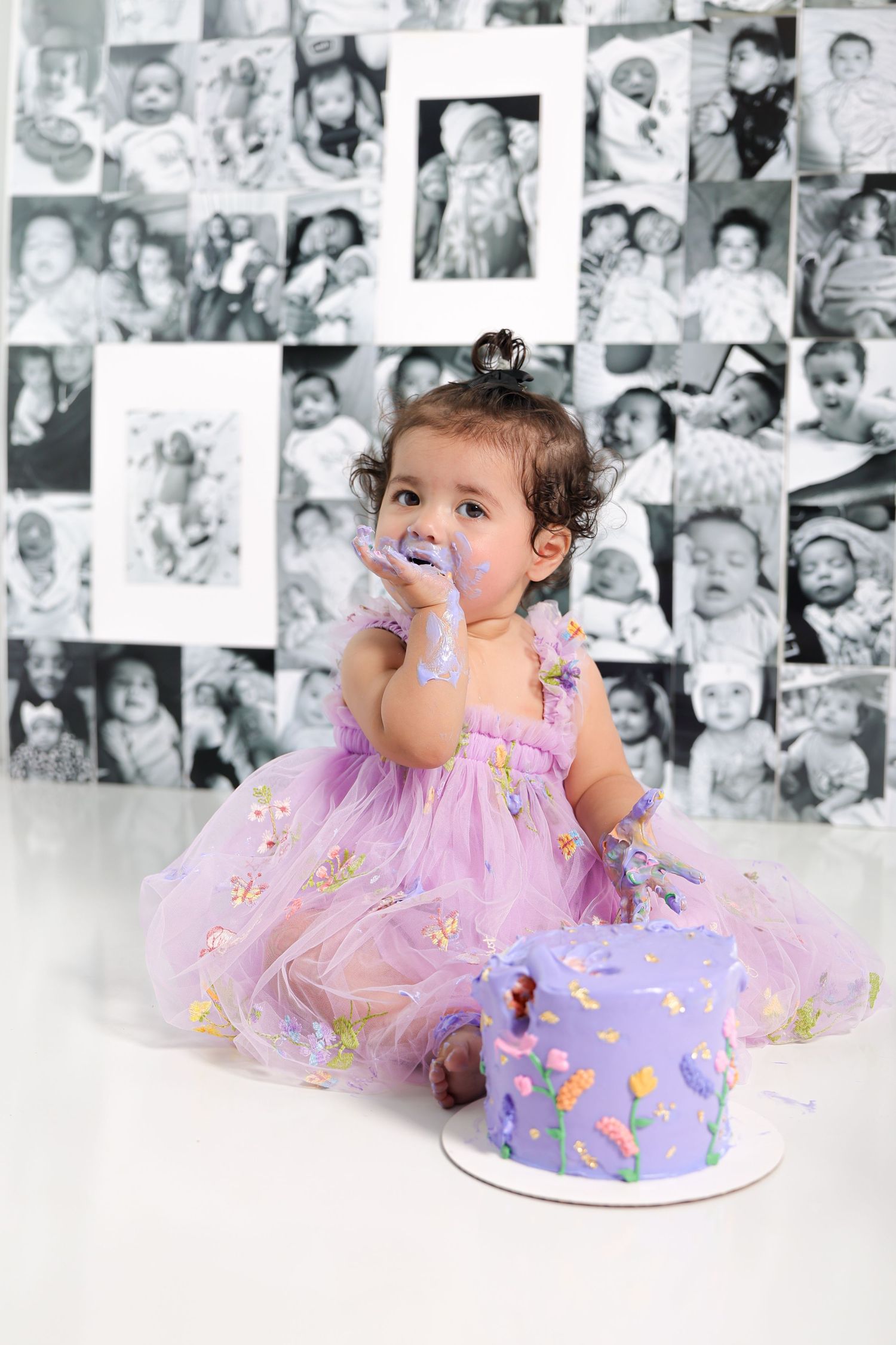Baby covered in purple frosting enjoys first birthday cake smash photoshoot.