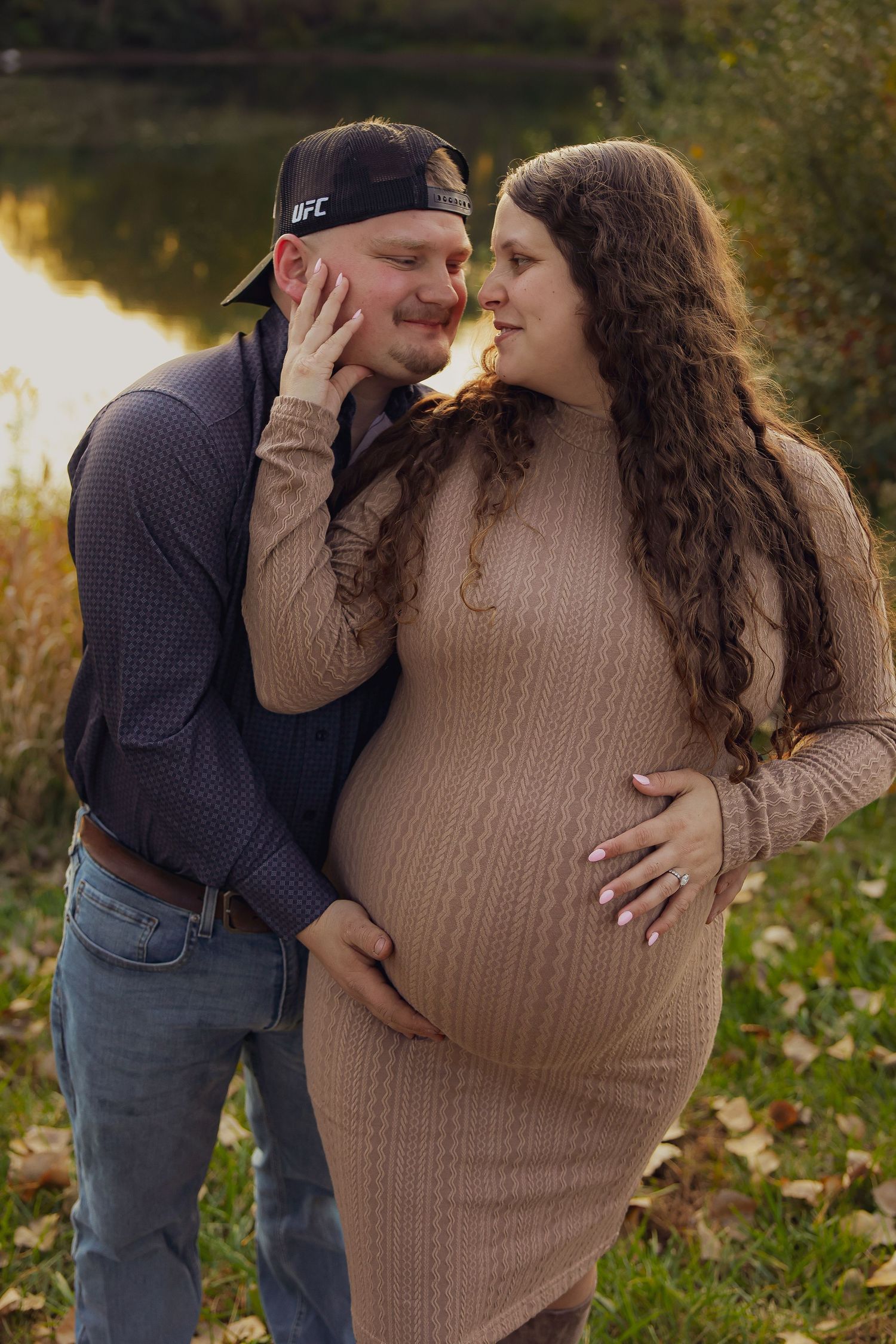 A couple shares an intimate moment by a lake during an autumn maternity photoshoot.