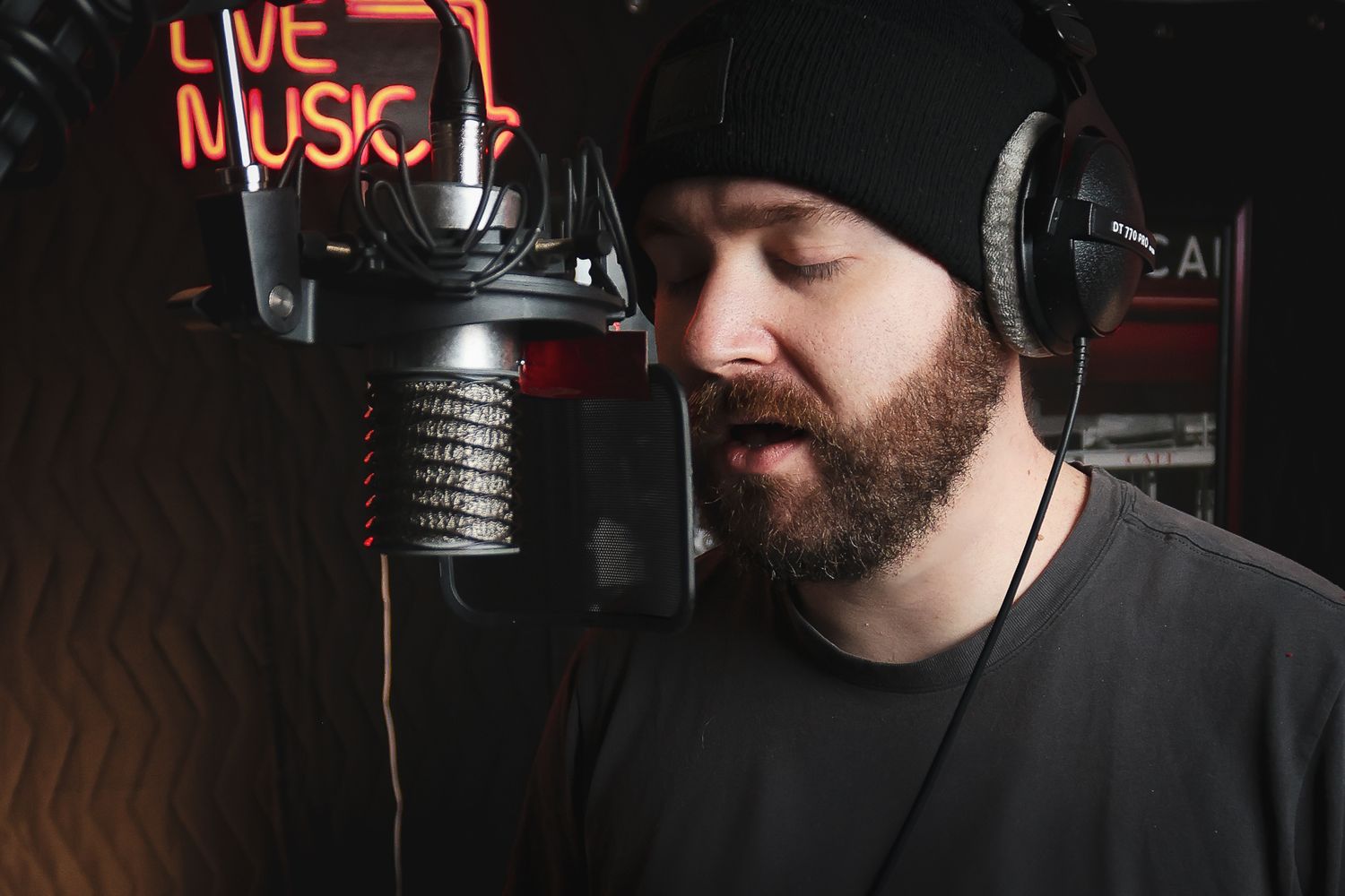 Music producer wearing headphones records vocals in a studio with neon live music sign.