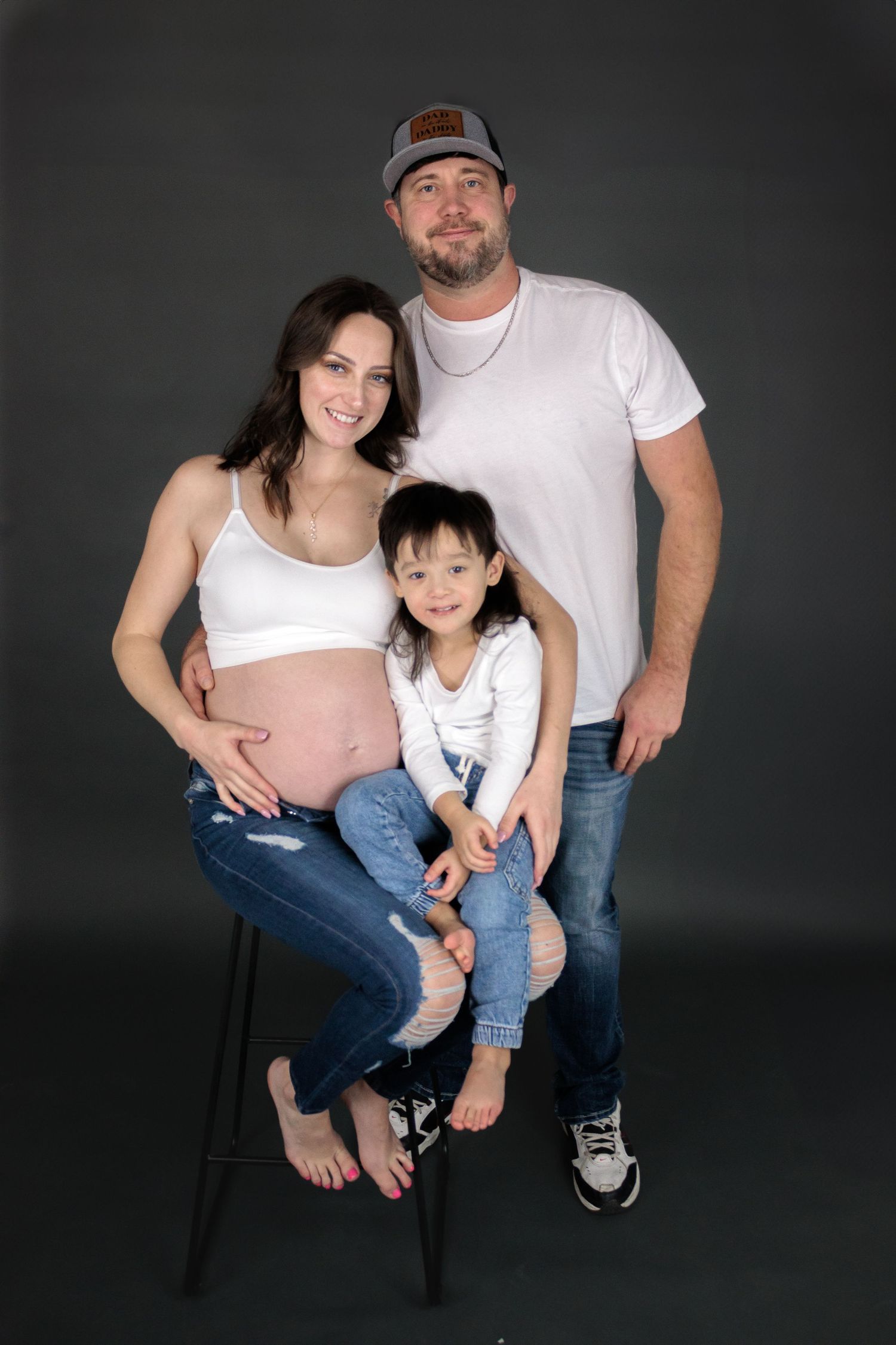 Family maternity photos on black backdrop showing parents and child.