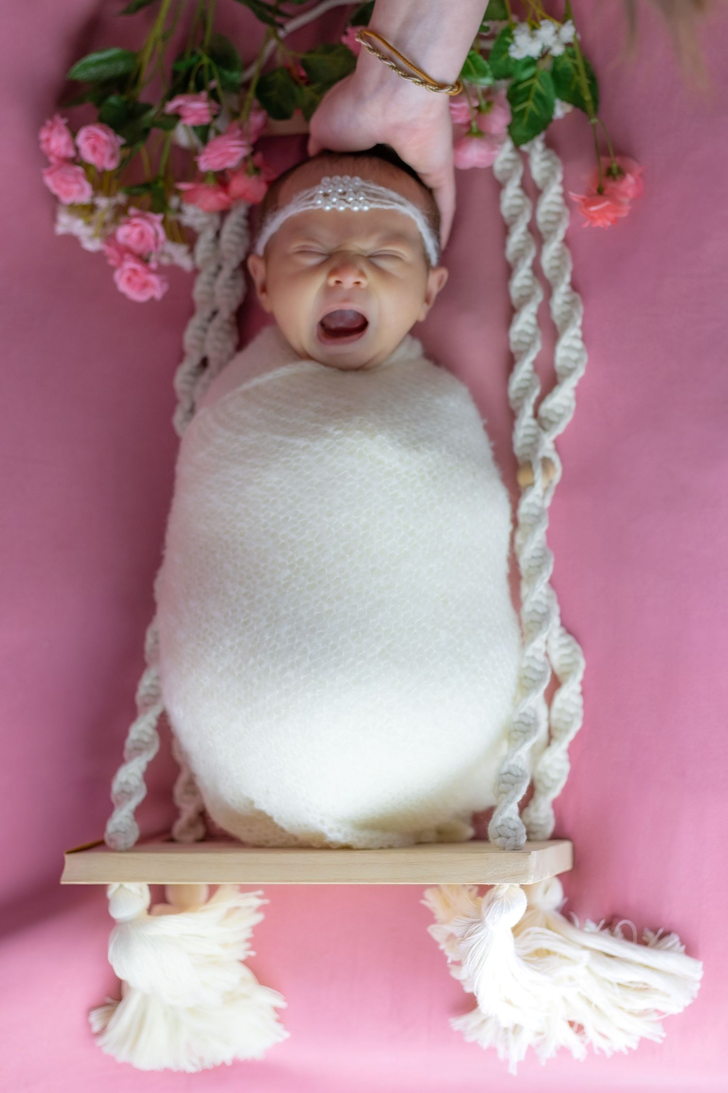 Baby photography scene with pink roses and white decorative swing on pink backdrop.
