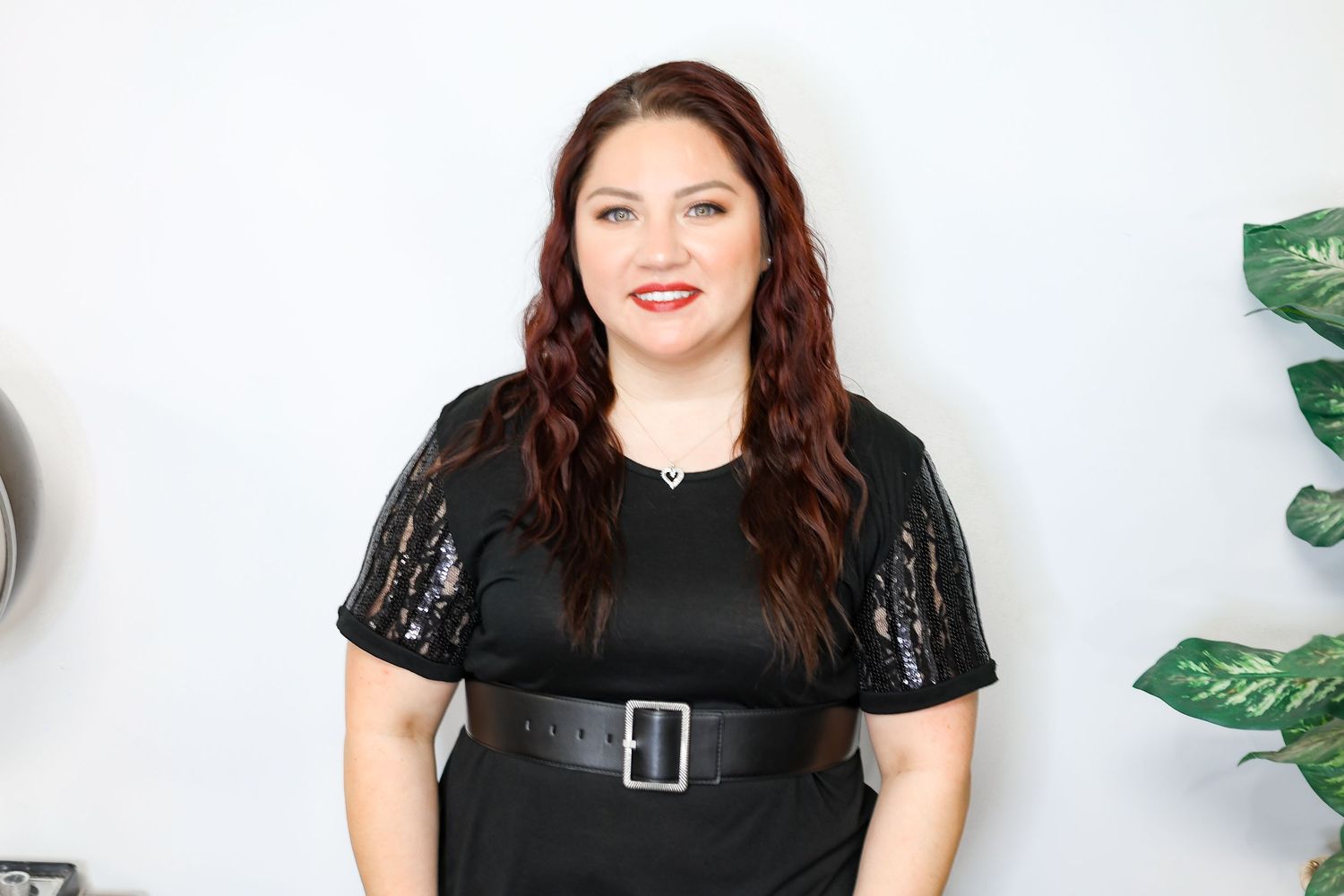 Hair professional showcasing styling techniques in black top against neutral background.