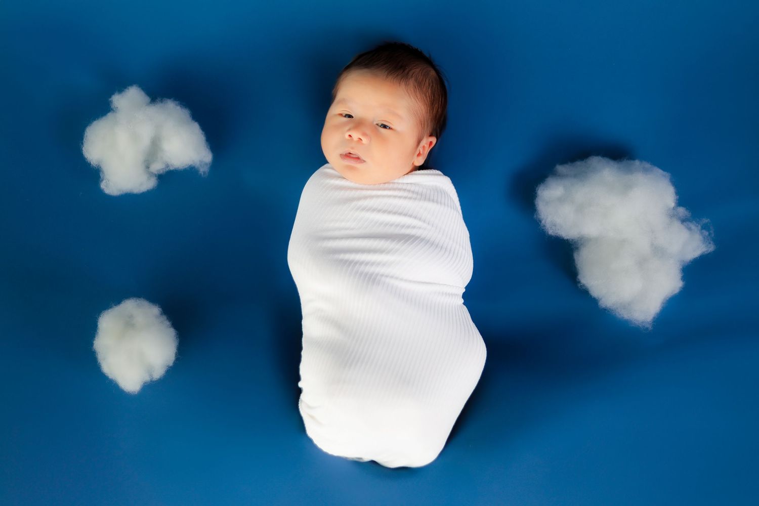 Sleeping newborn on blue background with white cotton cloud props.