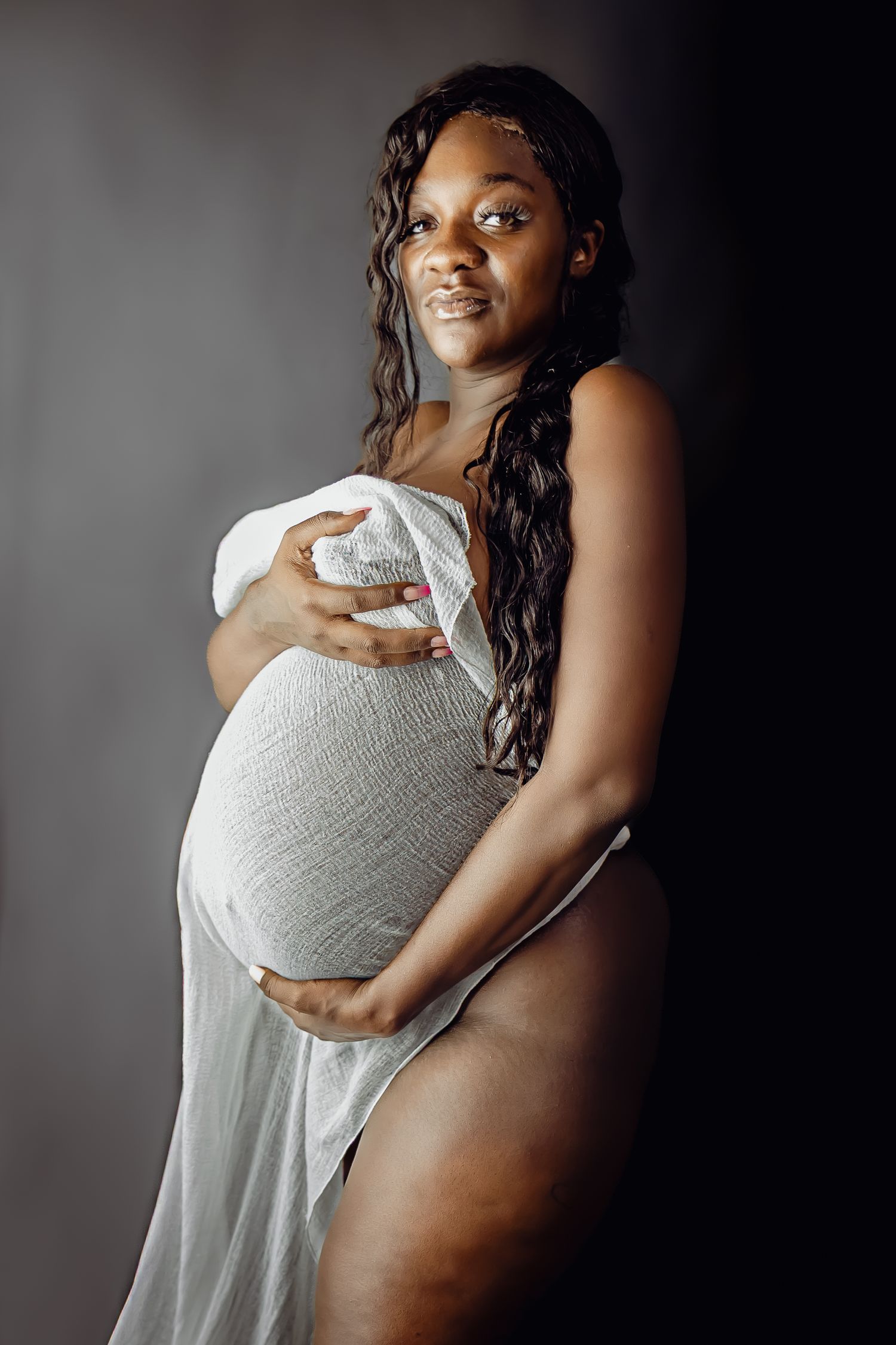 Side-view maternity portrait showing the beauty of pregnancy against dark background.