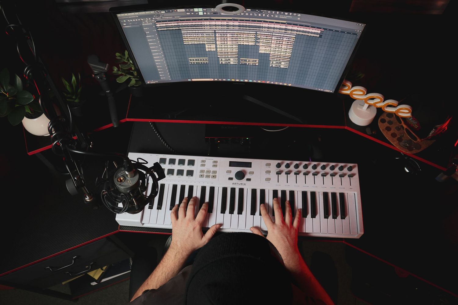 Hands playing MIDI keyboard controller with computer screen displaying music software in background.