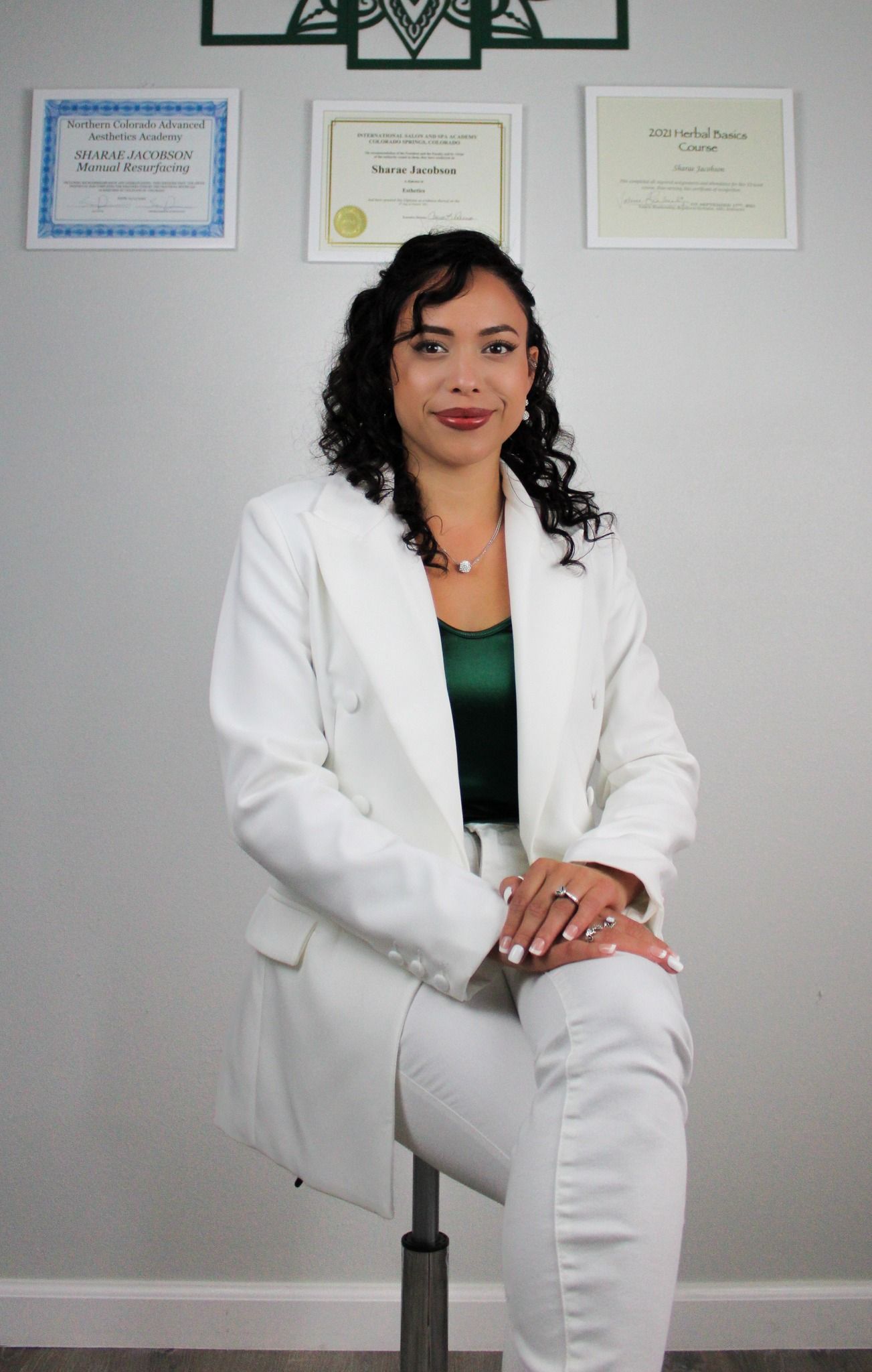 Professional seated portrait with certificates displayed on wall behind.