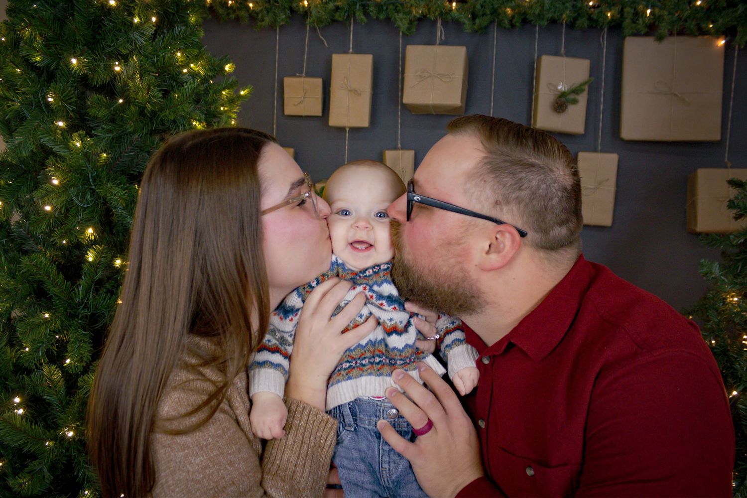 Family sharing joyful kisses and cuddles in front of a Christmas tree with twinkling lights.