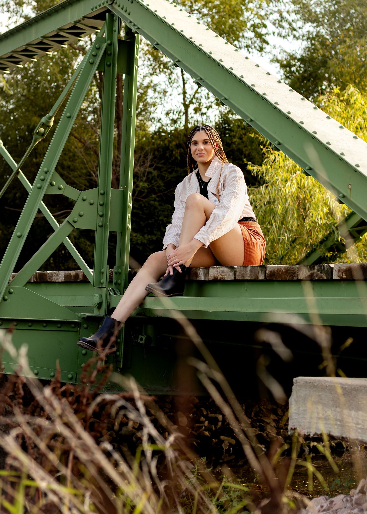 A stylish outfit with brown boots and a white blouse photographed on a green metal bridge structure in autumn.
