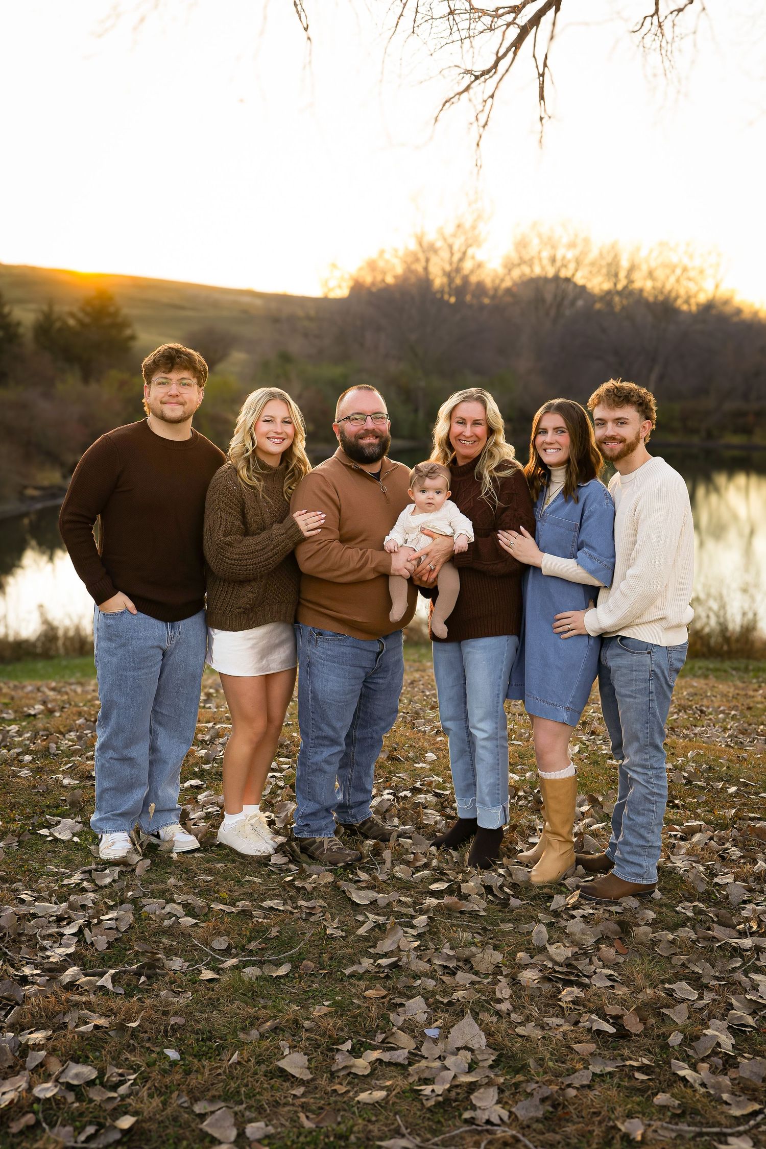 Group stands together by a lake at sunset on rocky ground covered in autumn leaves.