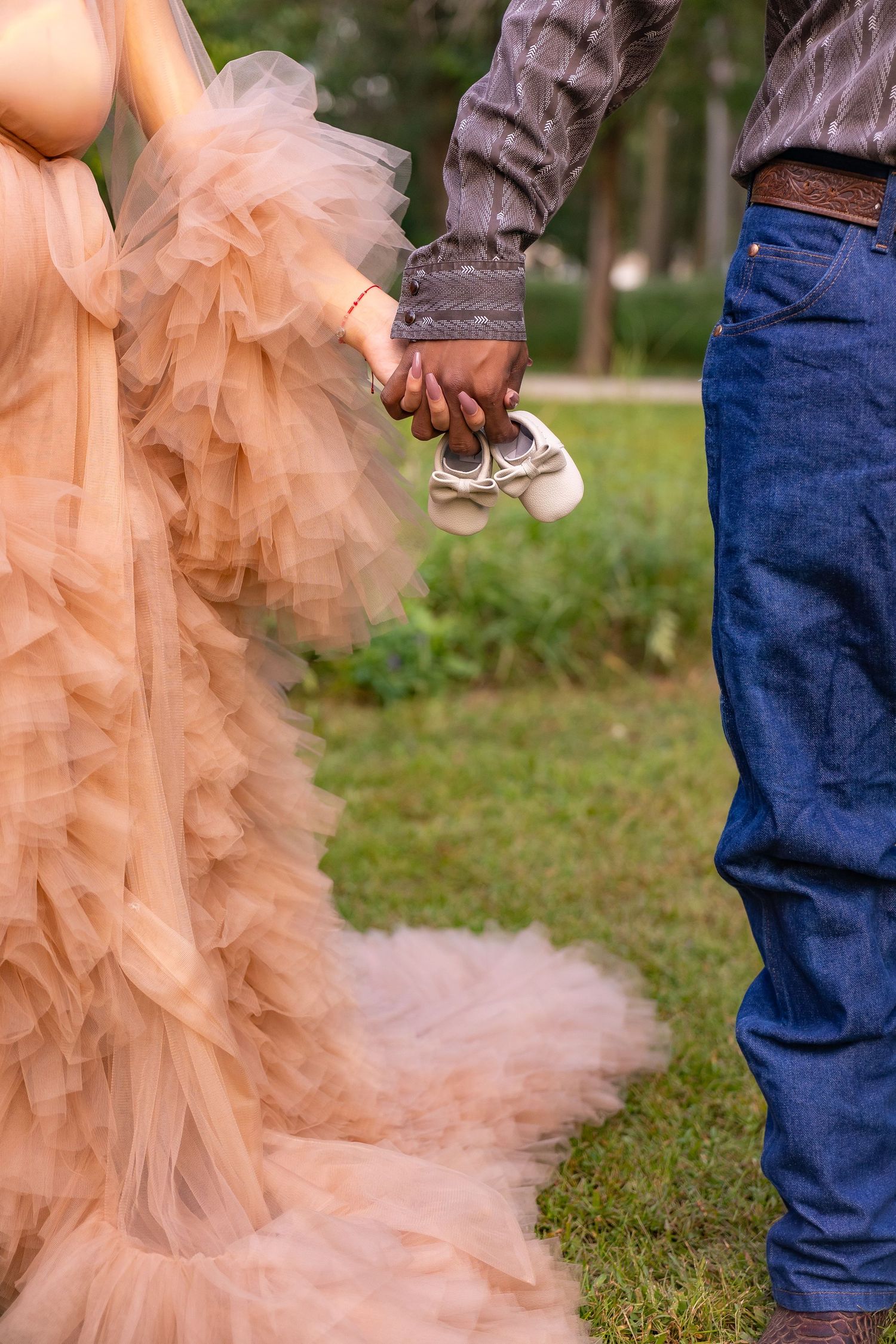 Close-up view of a couple holding hands with the bride wearing a flowing peach tulle dress against a grassy backdrop.
