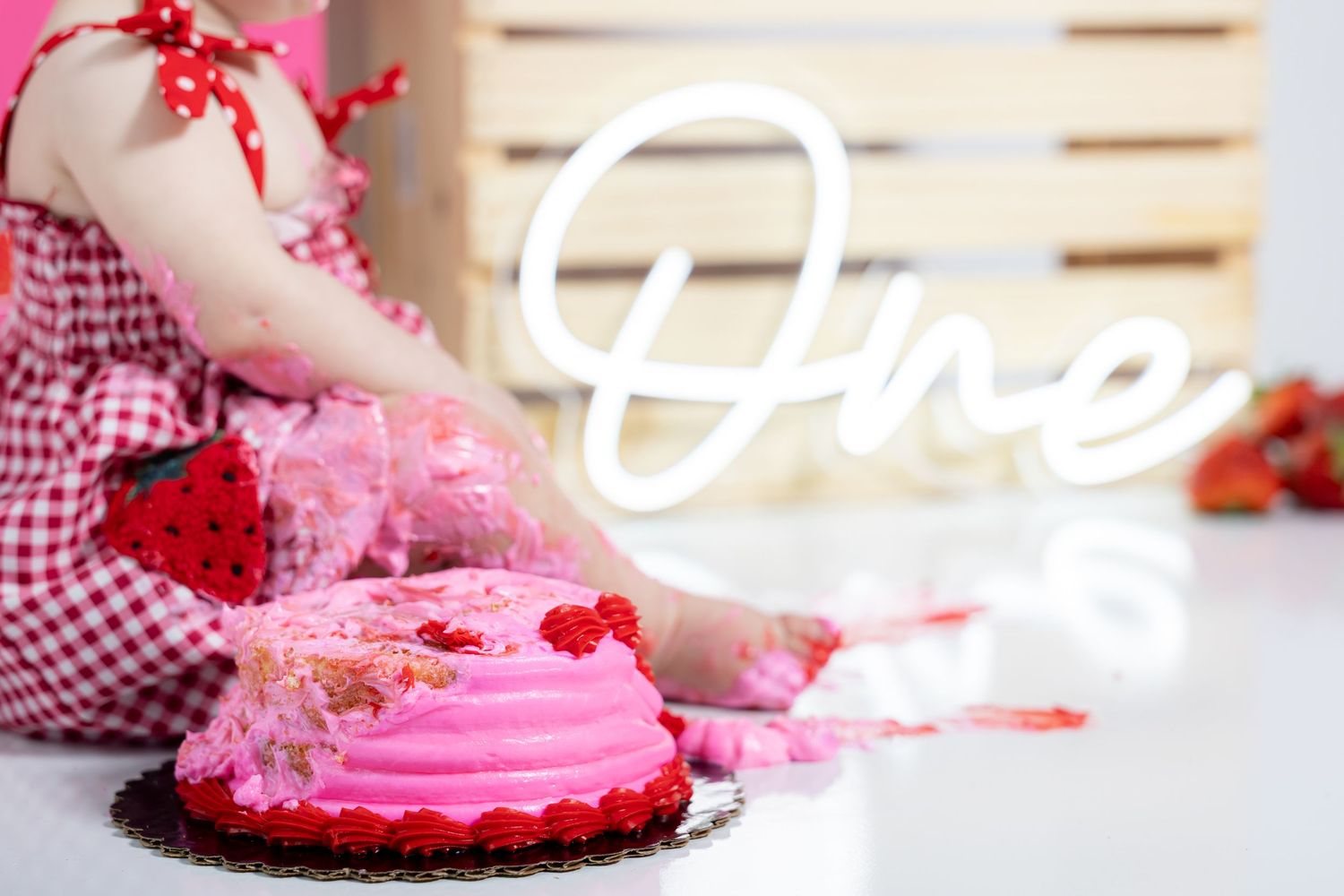 Pink frosted cake smash scene with decorative balloons and wooden accents.
