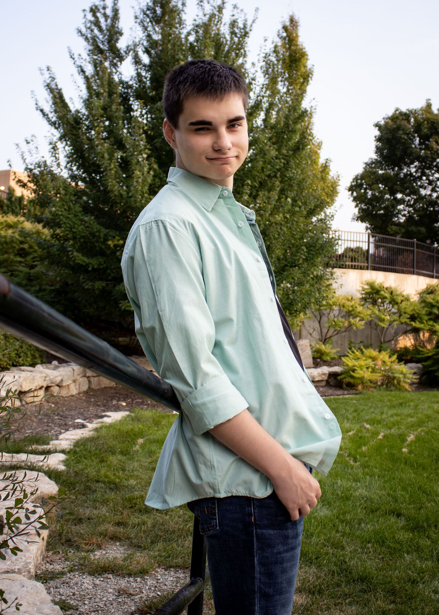 Casual outdoor poses in a mint shirt against a grassy landscape with trees.
