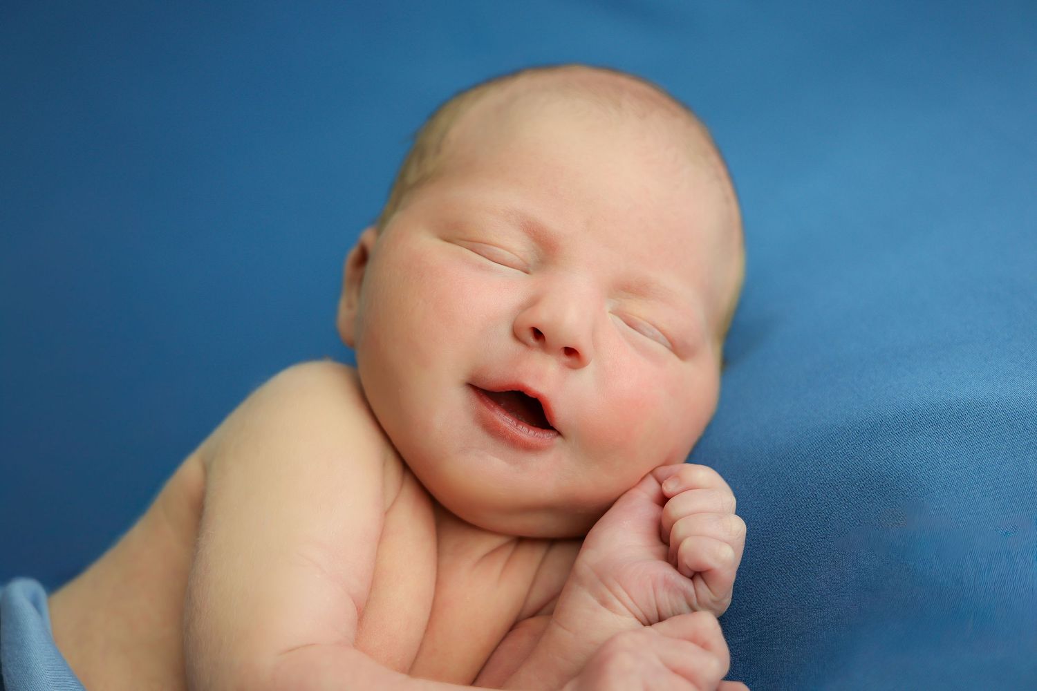 Sleeping newborn baby photographed in soft lighting against a blue background.