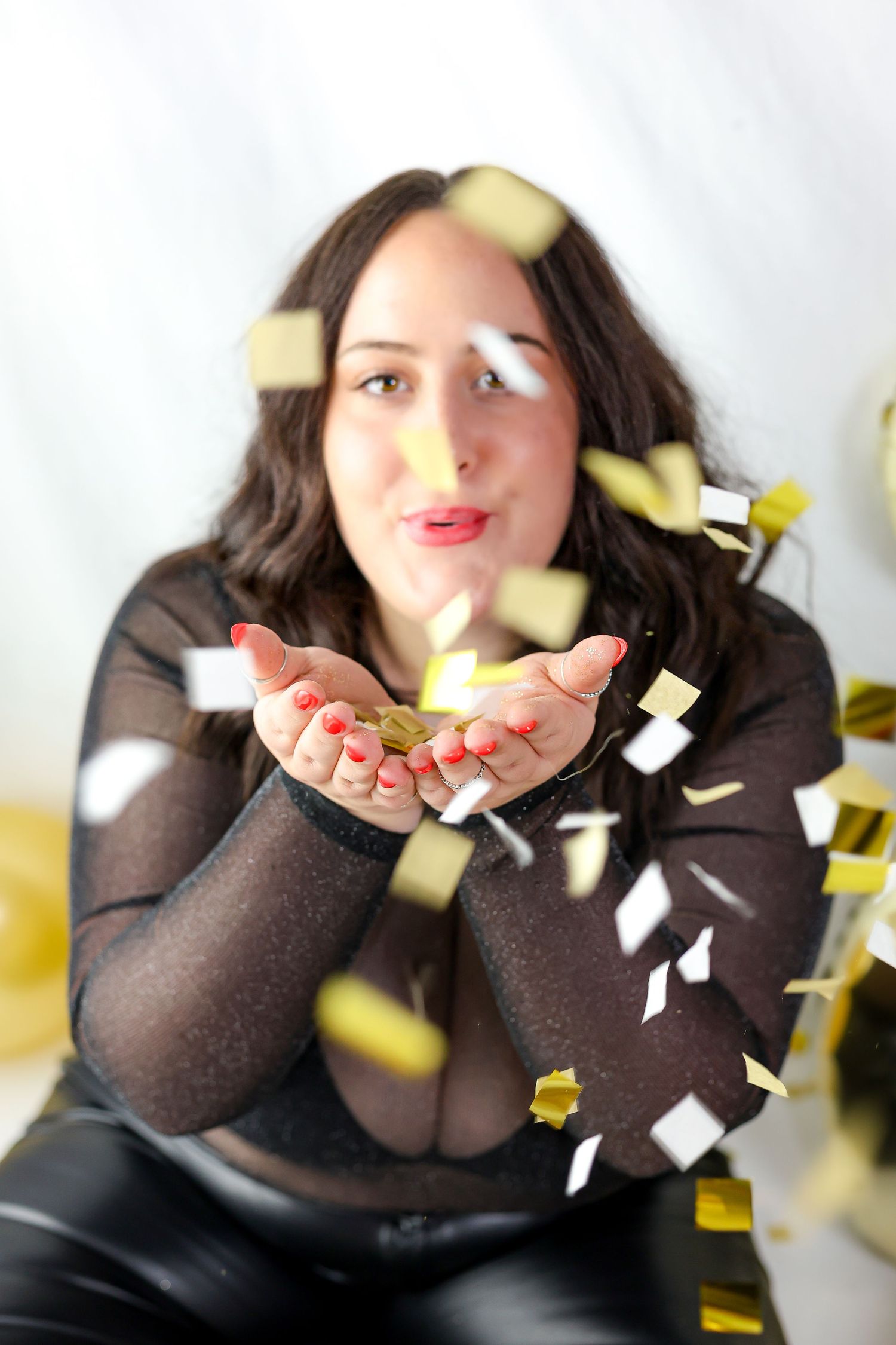 Person in dark sweater playfully blowing gold and white confetti from cupped hands in sequence of photos.