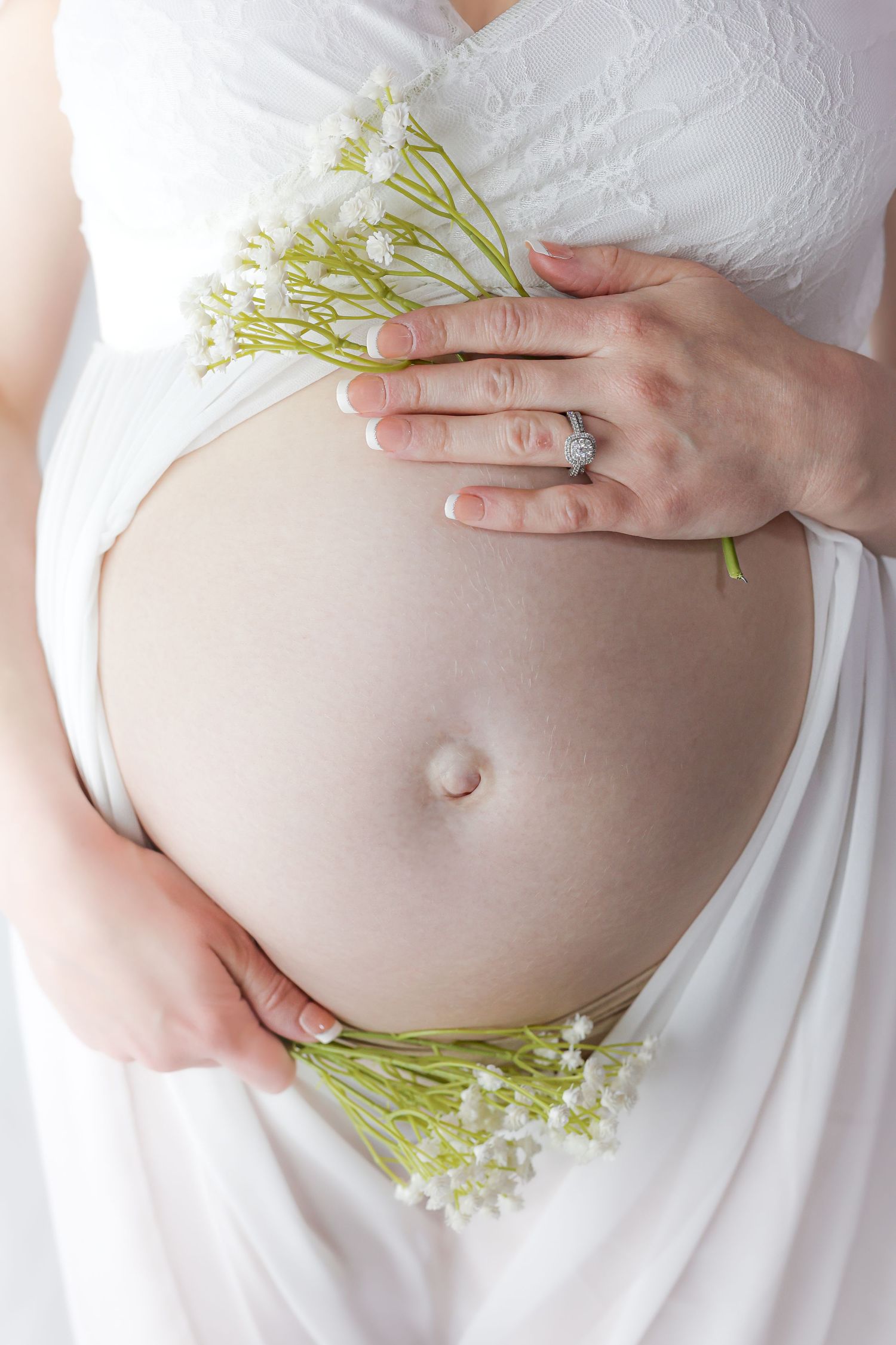 Close-up of pregnant belly with delicate white flowers and wedding ring.