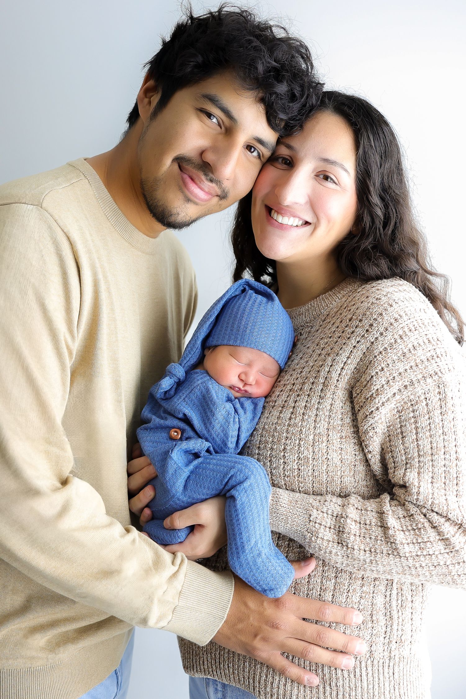 A couple in neutral sweaters cuddles with their newborn baby wearing blue in a series of tender family portraits.
