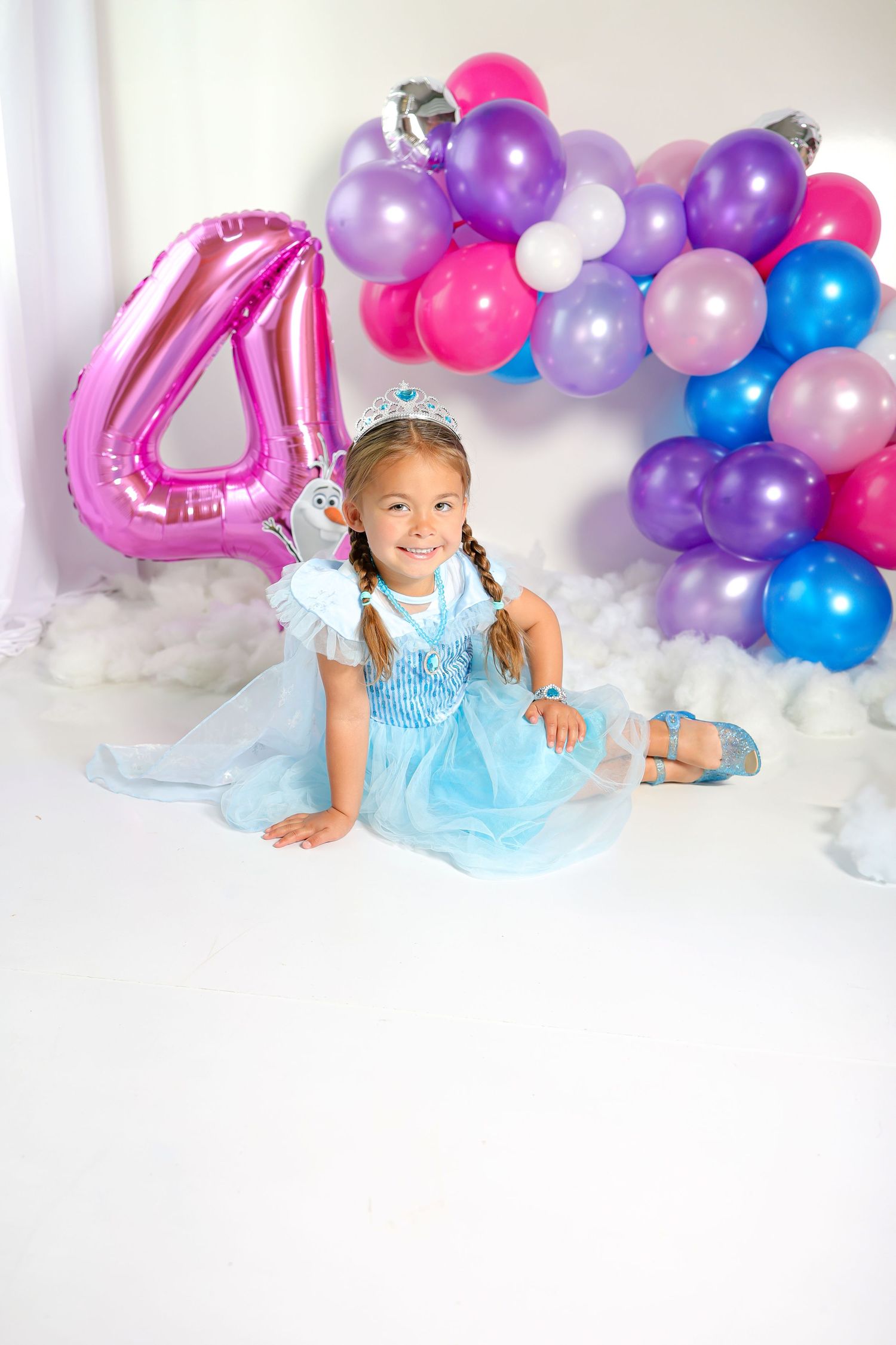 Birthday photoshoot setup with blue and purple balloon garland and sparkly decorations against white backdrop.
