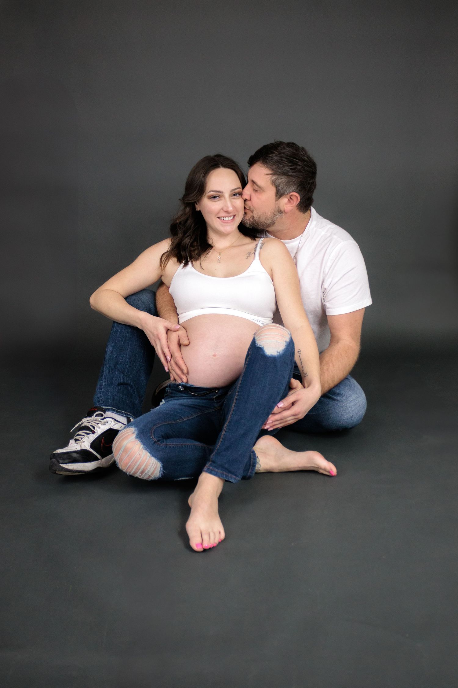 Relaxed maternity photos showing couple lounging together on dark floor.