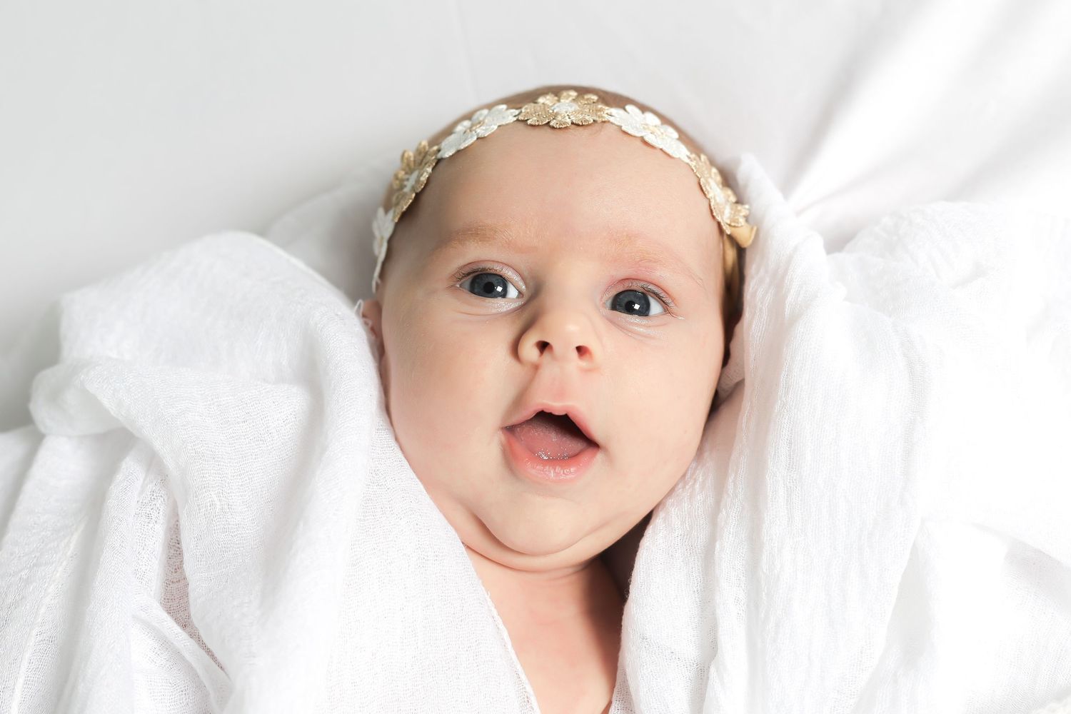 Baby with floral headband making expressive face against white background.