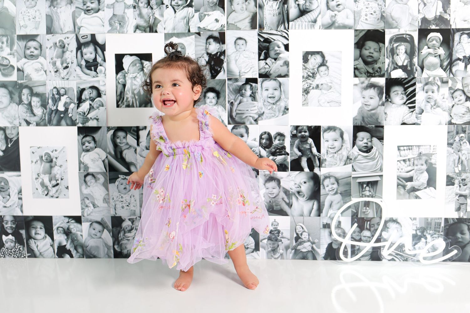Baby in pink dress laughs during cake smash session with vintage photo backdrop.