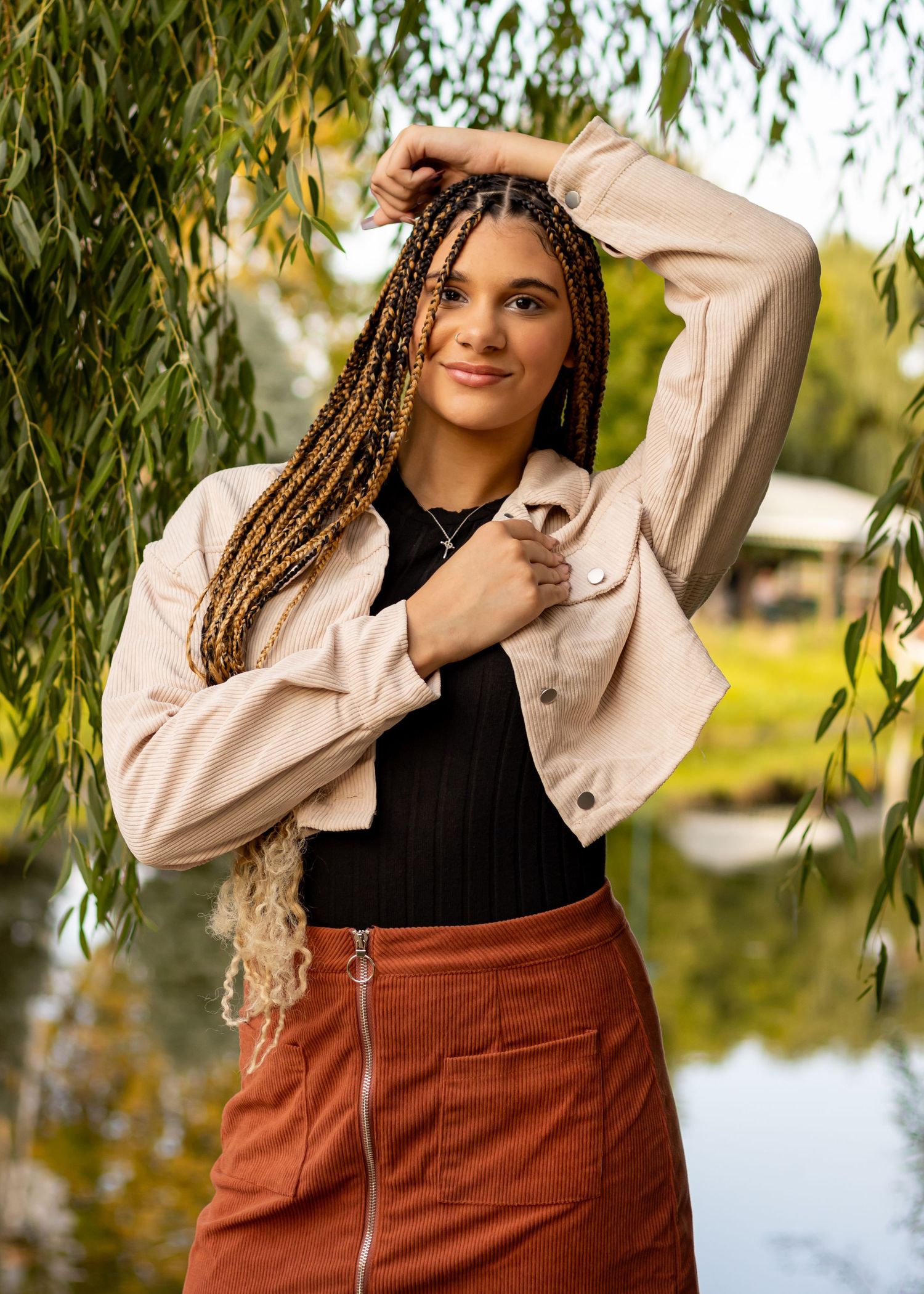 Fashion portrait by water featuring white denim jacket and rust-colored corduroy outfit.
