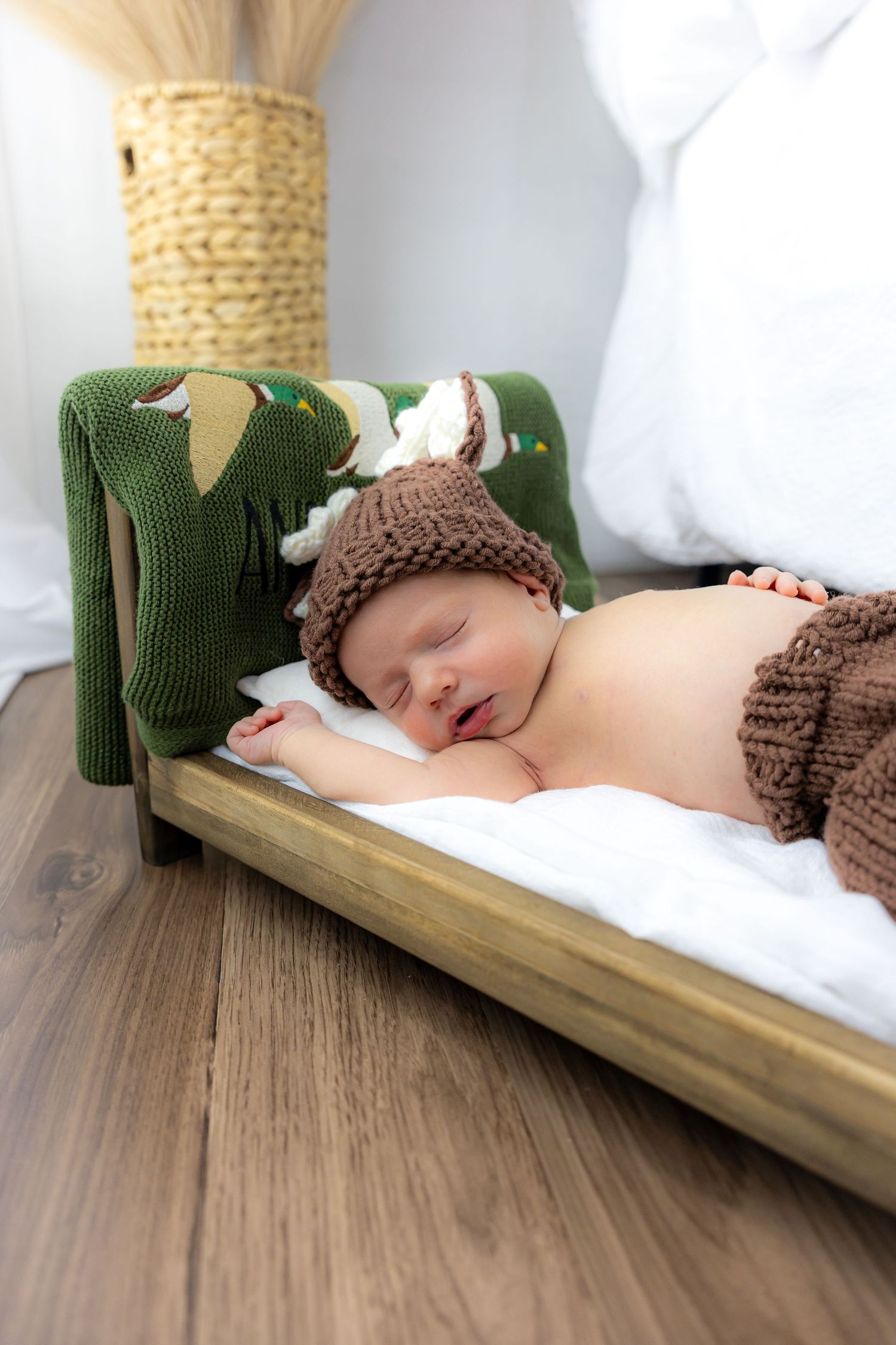 A sleeping baby wearing a knit brown and green dinosaur outfit lying on a wooden surface.