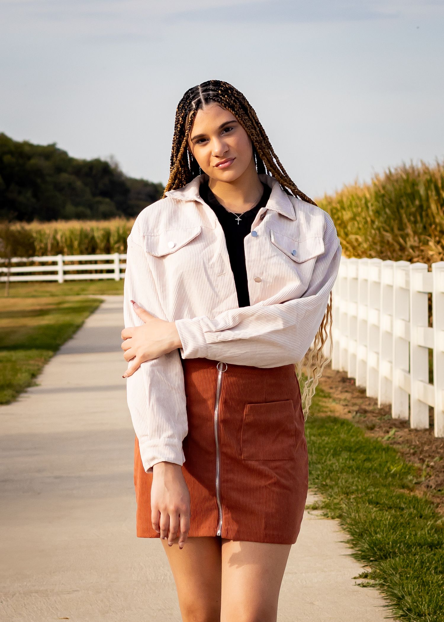 Outdoor fashion shoot featuring white shirt and brown corduroy skirt along white fence pathway.