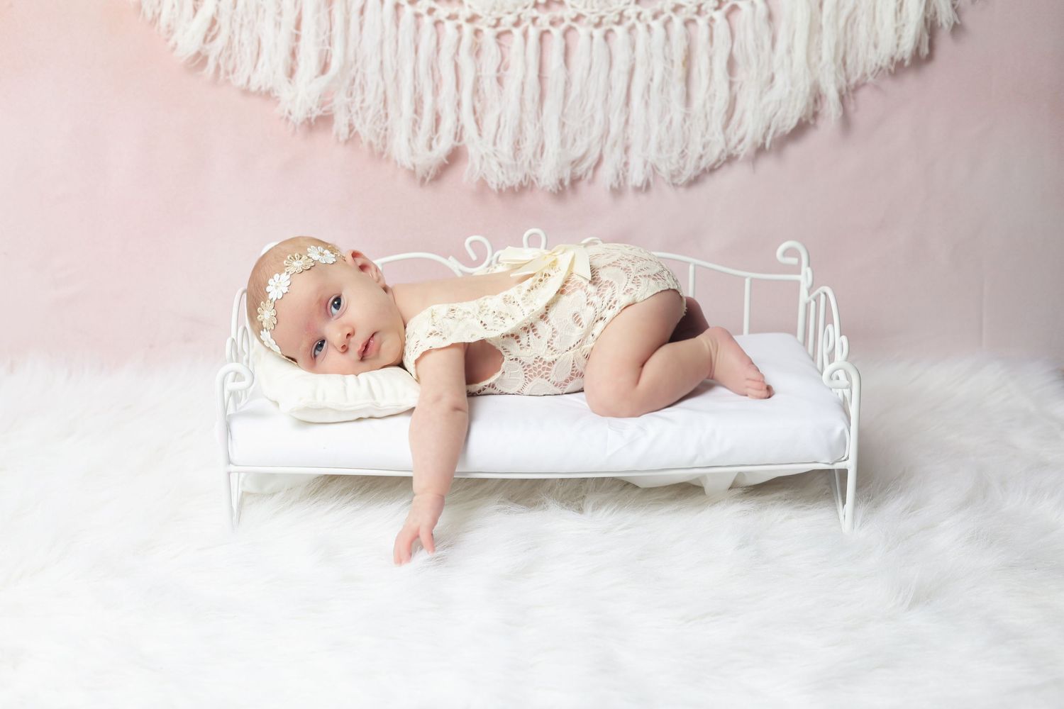 Newborn photography setup with white bedding and decorative elements on a pink background.