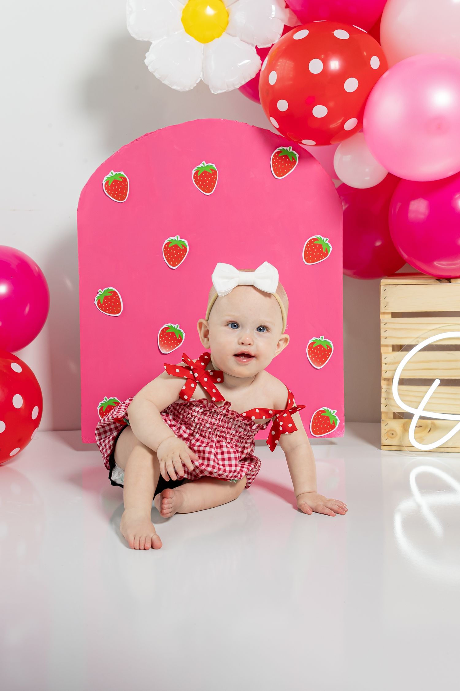 Pink and white party setup with strawberry decorations and balloons against light background.