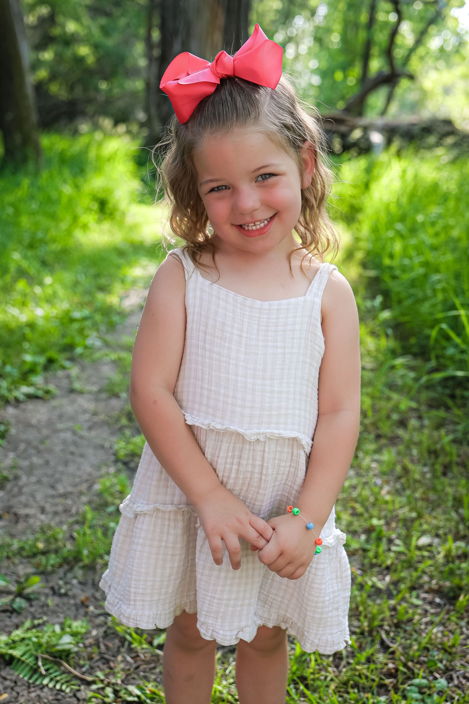 A child in a white gingham dress with a red bow plays joyfully in a wooded setting.
