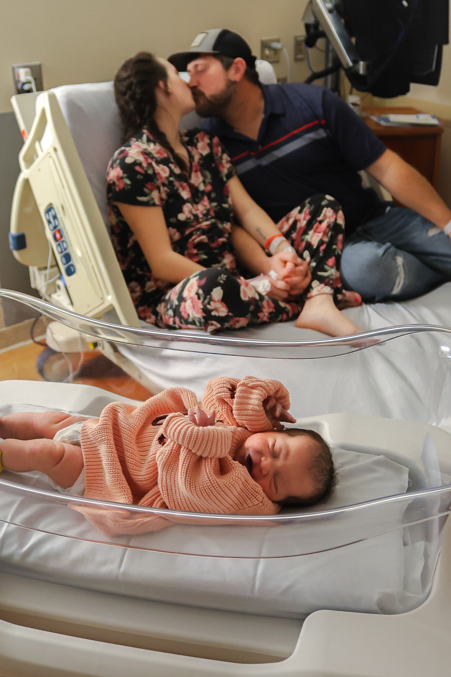 Side view of newborn in peach sweater resting in hospital bassinet.