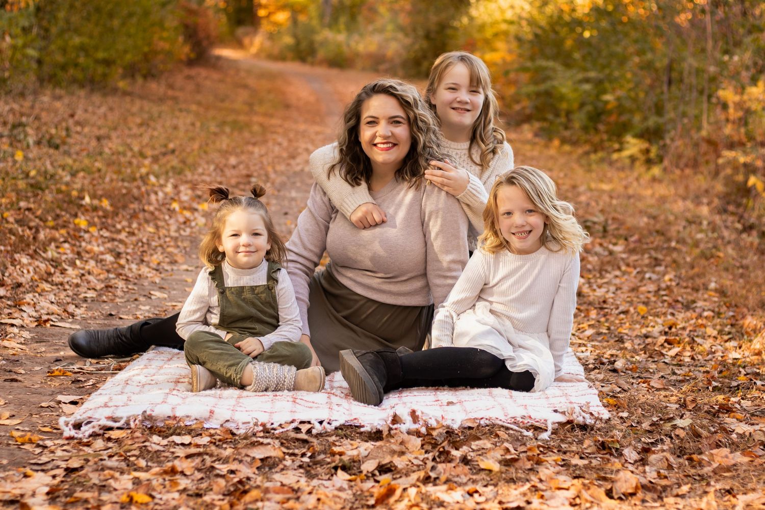 Autumn family photo session with group sitting on blanket among fallen leaves.