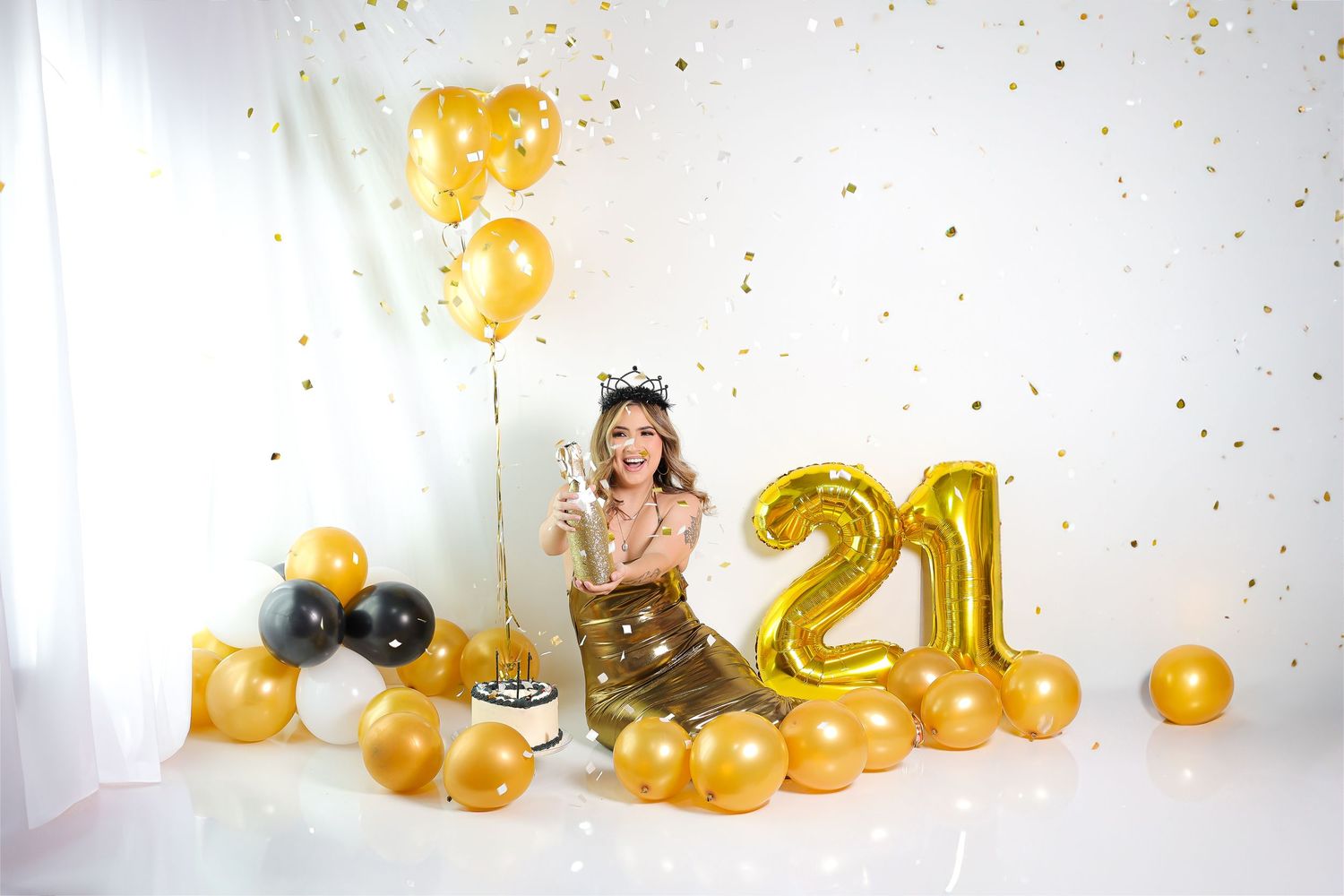 Festive celebration setup with gold and black balloons, number 21 balloon decorations, and confetti against white backdrop.