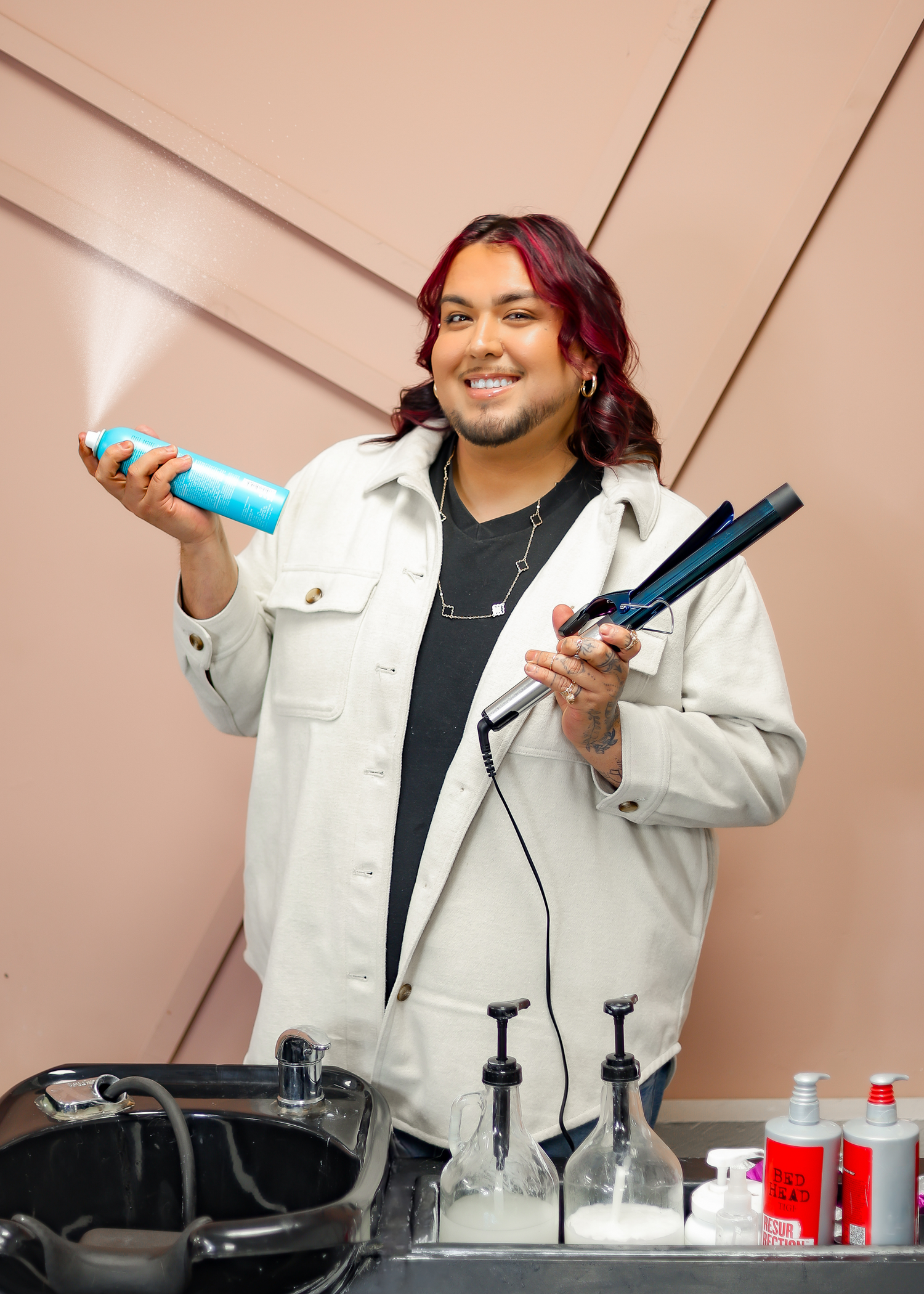 Stylist demonstrating various hair care products and tools in white denim jacket.