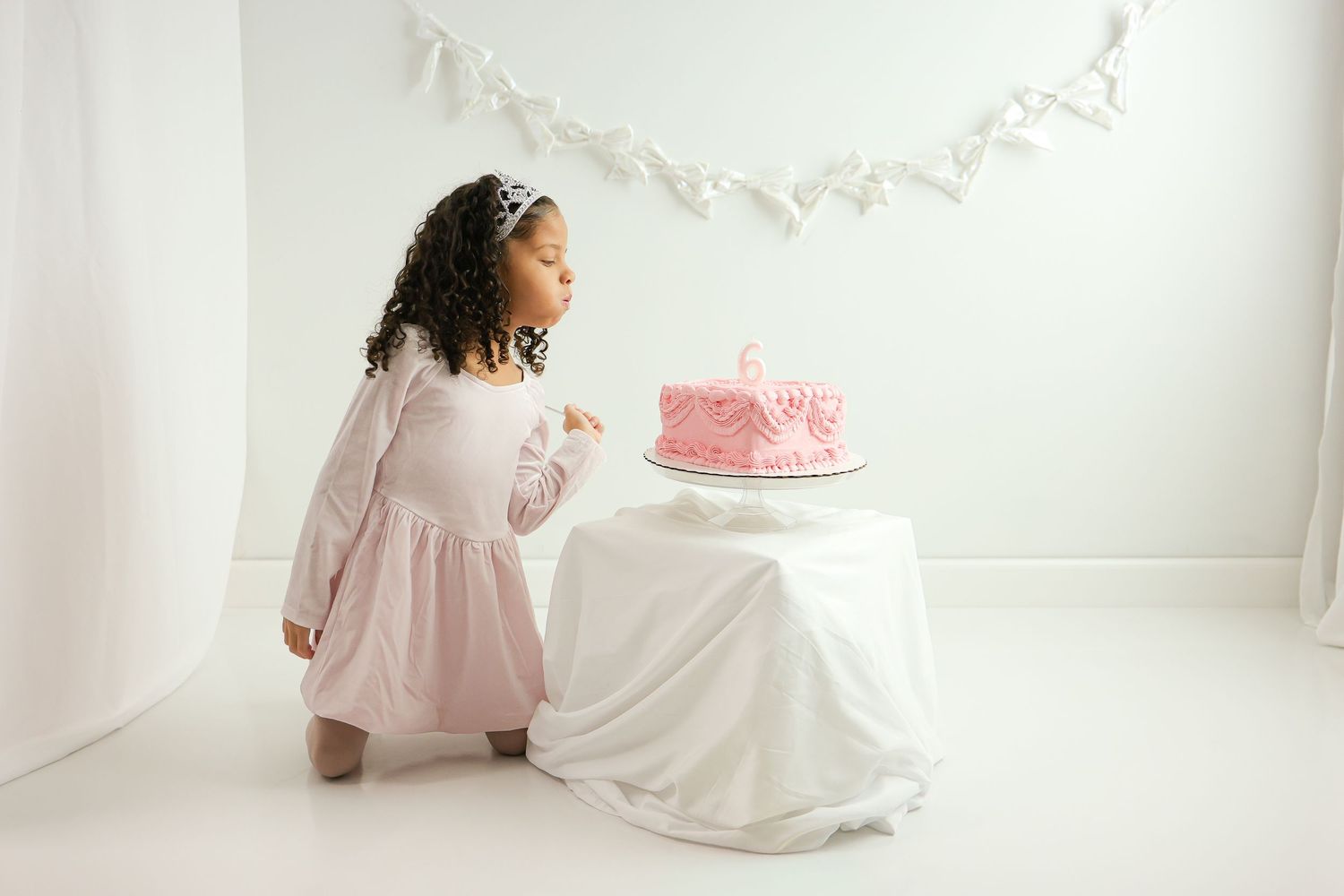 A dreamy photo series showing someone in a white dress sitting near a pink birthday cake against a light backdrop.