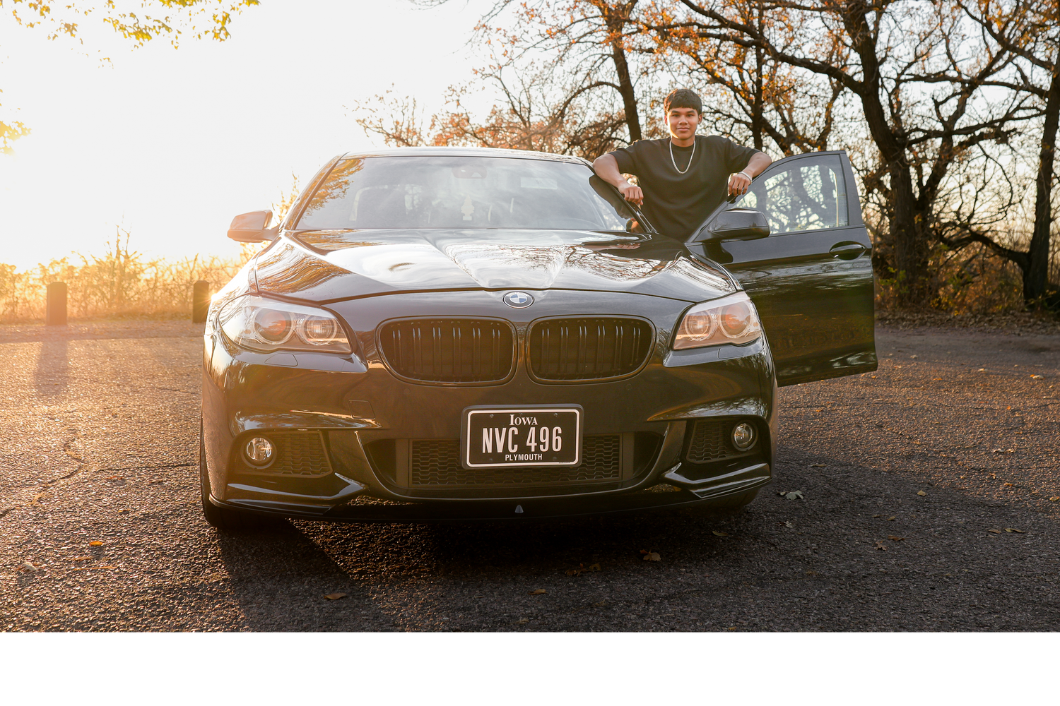 A black BMW M5 parked on gravel during golden hour sunset with someone sitting on the hood.