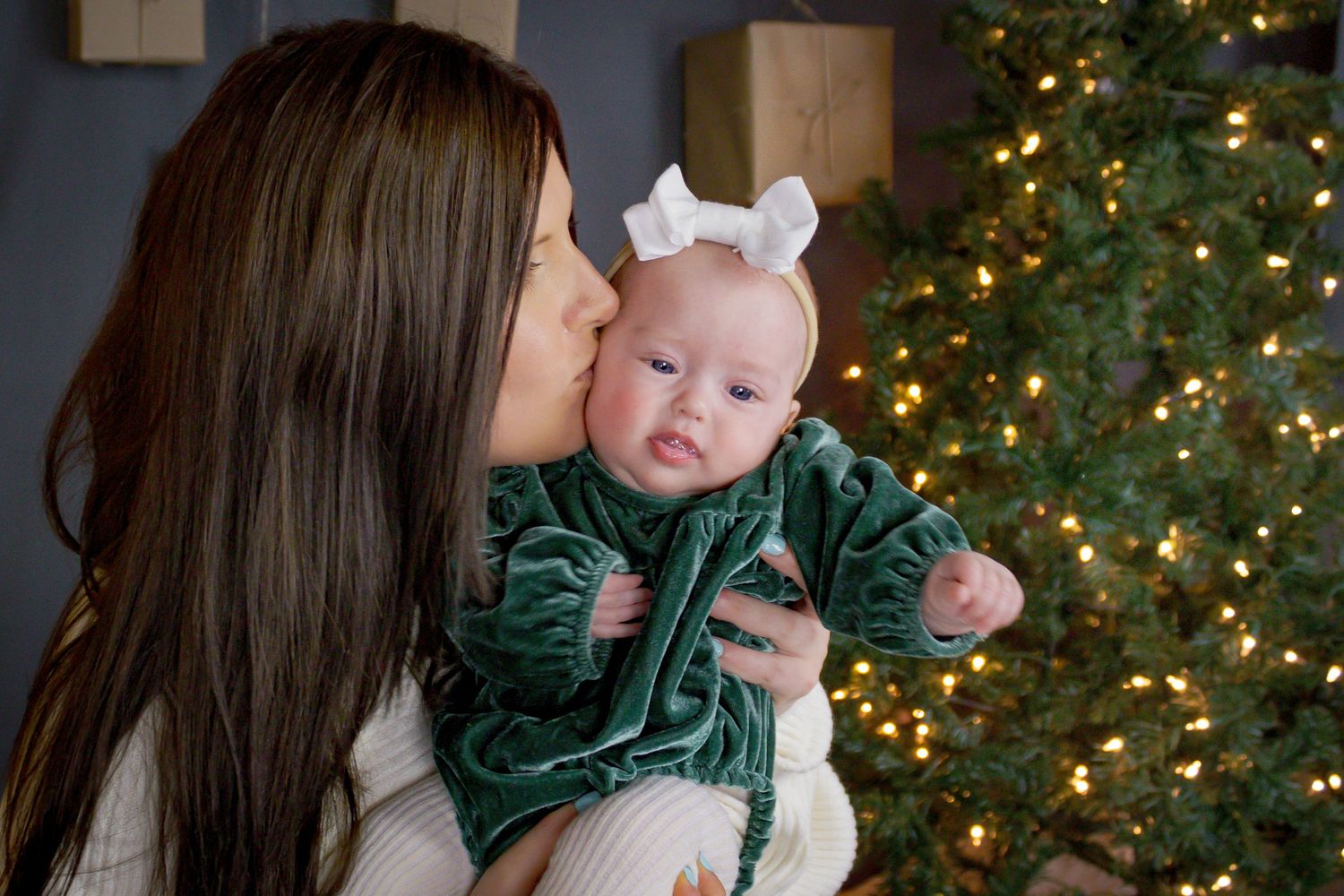 Holiday portraits with baby in green velvet dress against lit Christmas tree background.