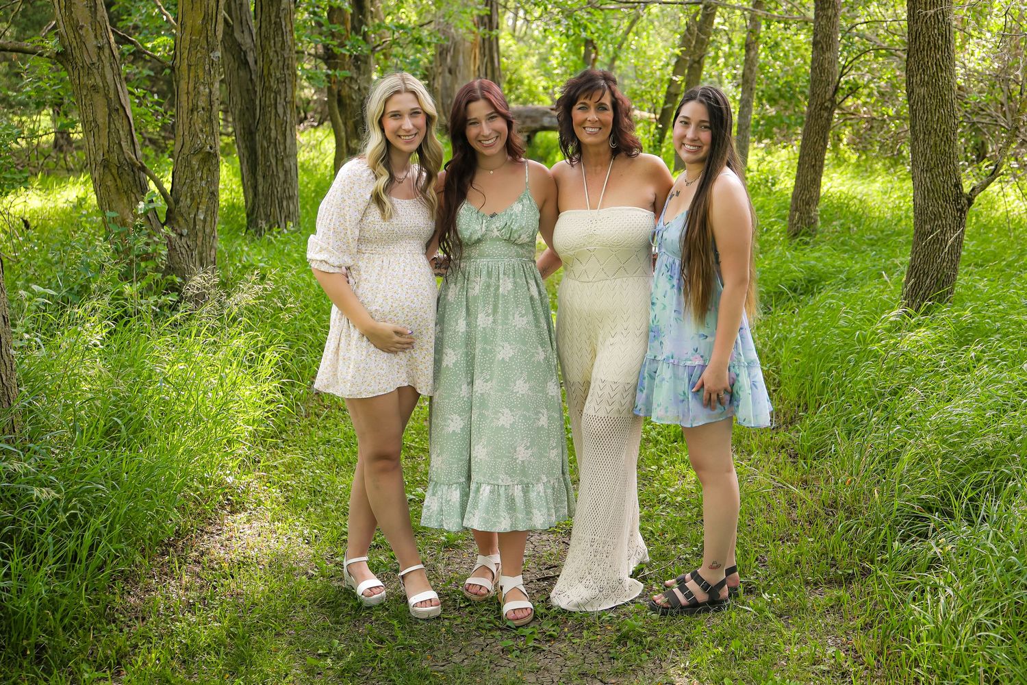 Group photo of people wearing pastel dresses in a sunlit wooded area.