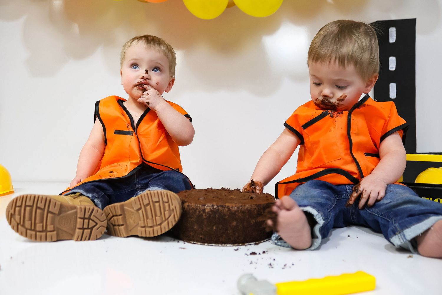 Construction zone cake smash setup with yellow balloons and safety equipment.