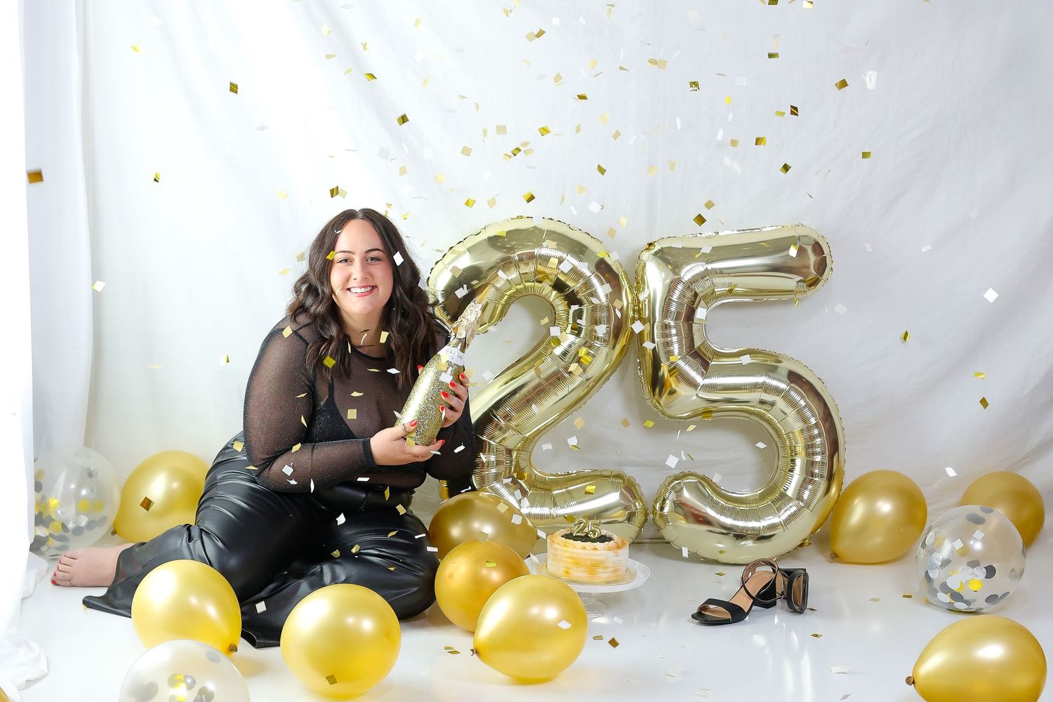 A celebratory scene with gold number 25 balloons, gold confetti, and decorative elements against a white backdrop.